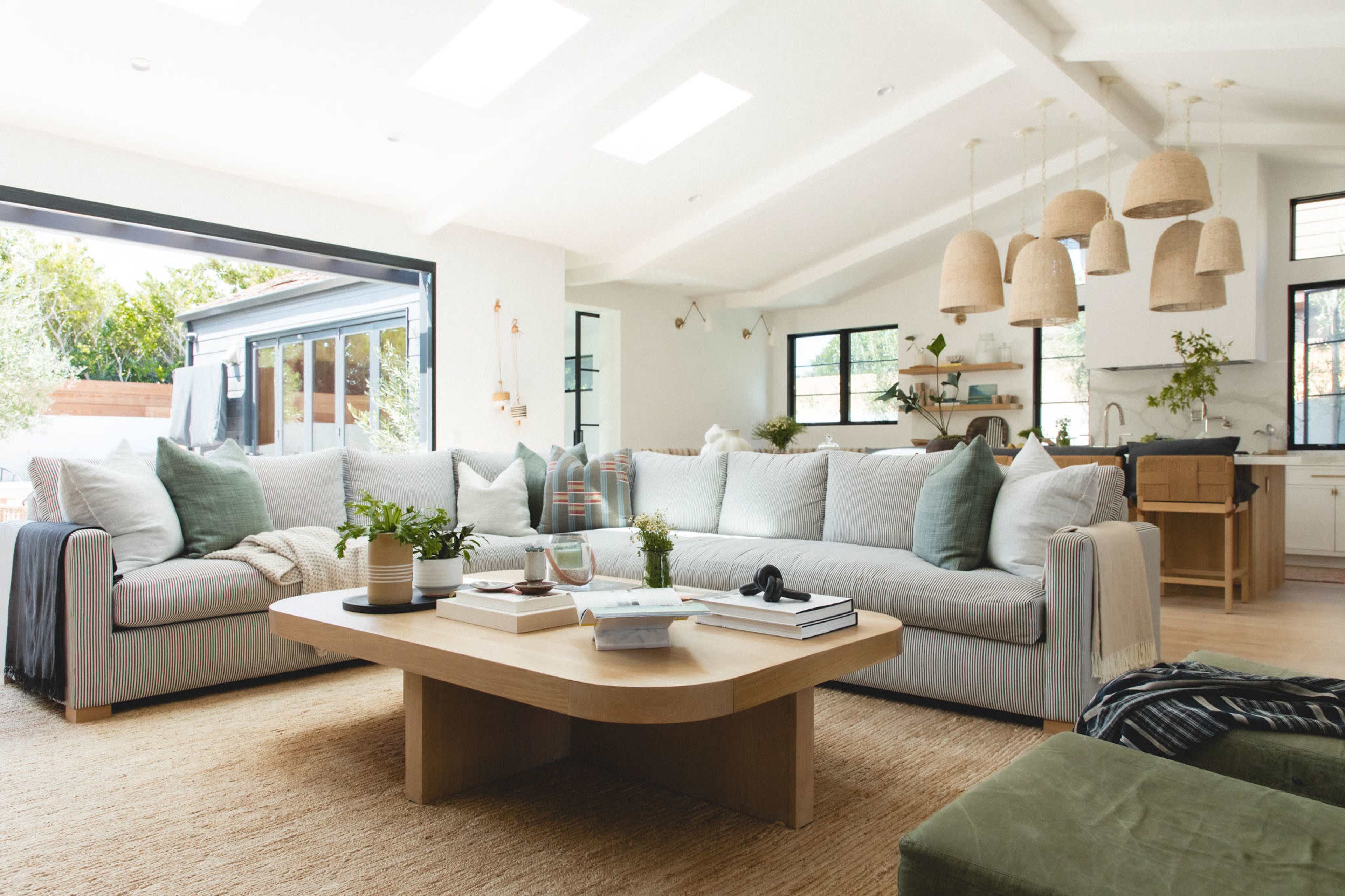 The image shows a bright living room with a large, light-colored sofa, a wooden coffee table, and pendant lighting hanging from the ceiling.