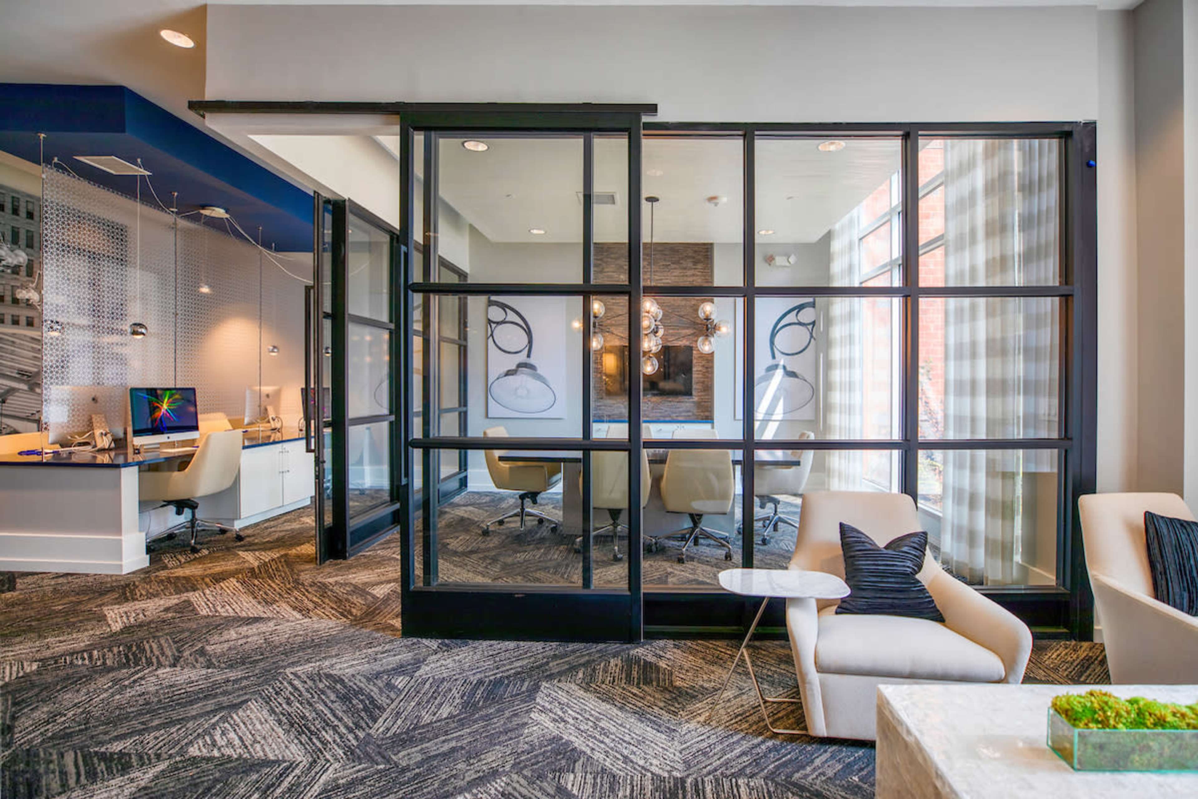 A modern office space with glass-panelled doors leading to a conference room, featuring contemporary furniture and a patterned carpet.