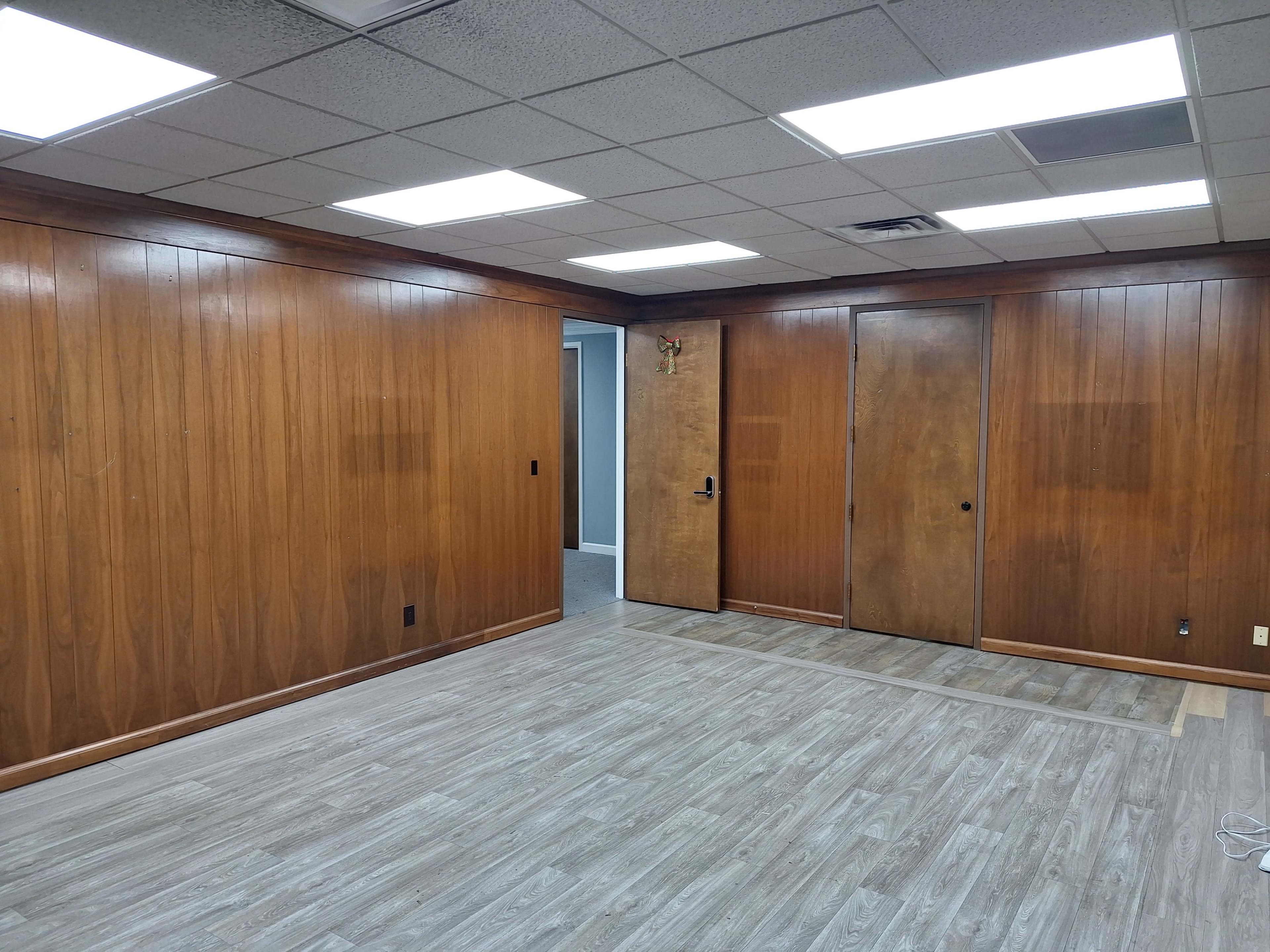 The image shows an empty room with wooden paneling on the walls, a gray floor, and two closed doors.