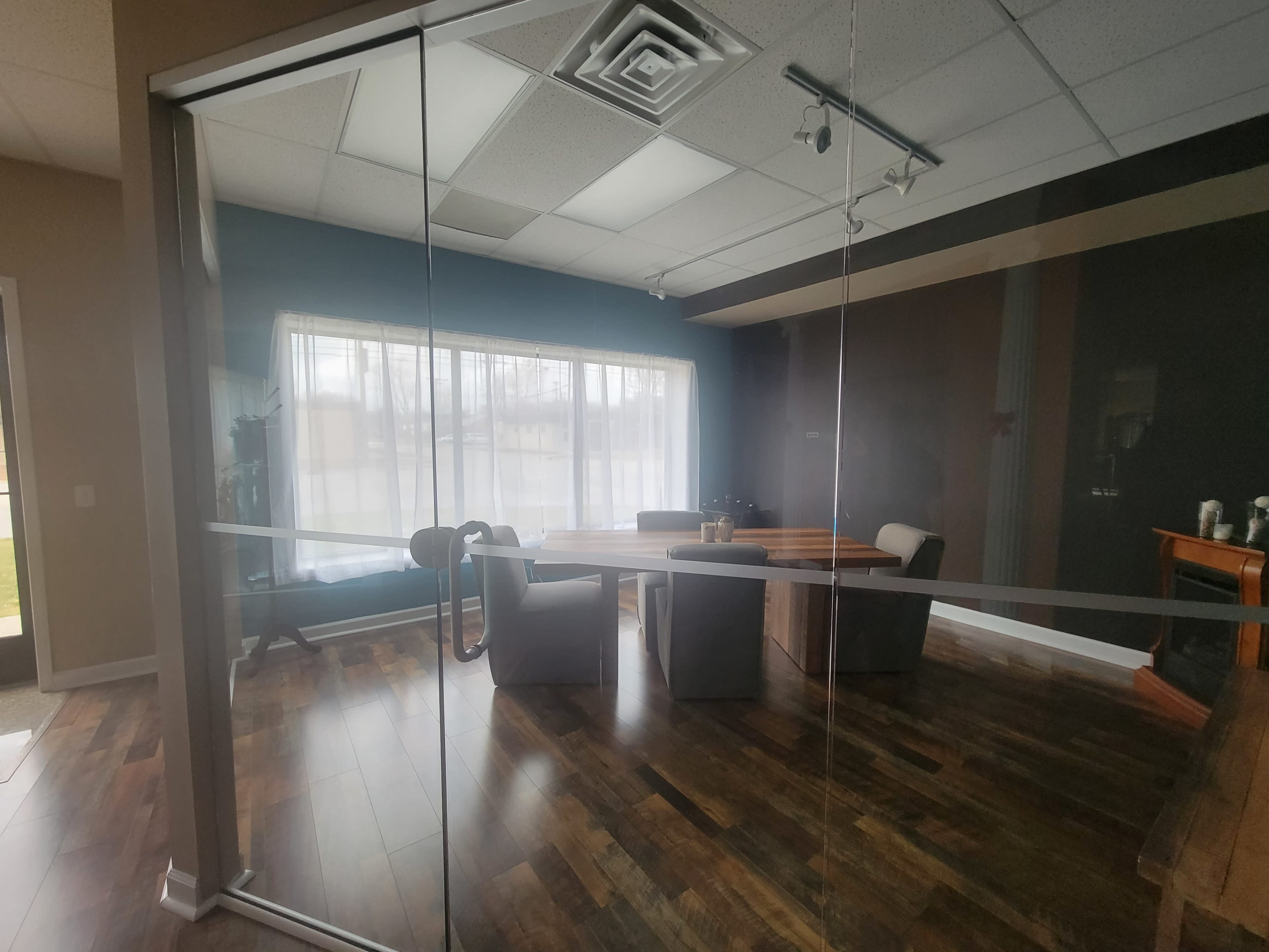 A conference room with a large wooden table and several chairs is visible through a glass wall, illuminated by natural light from a nearby window.