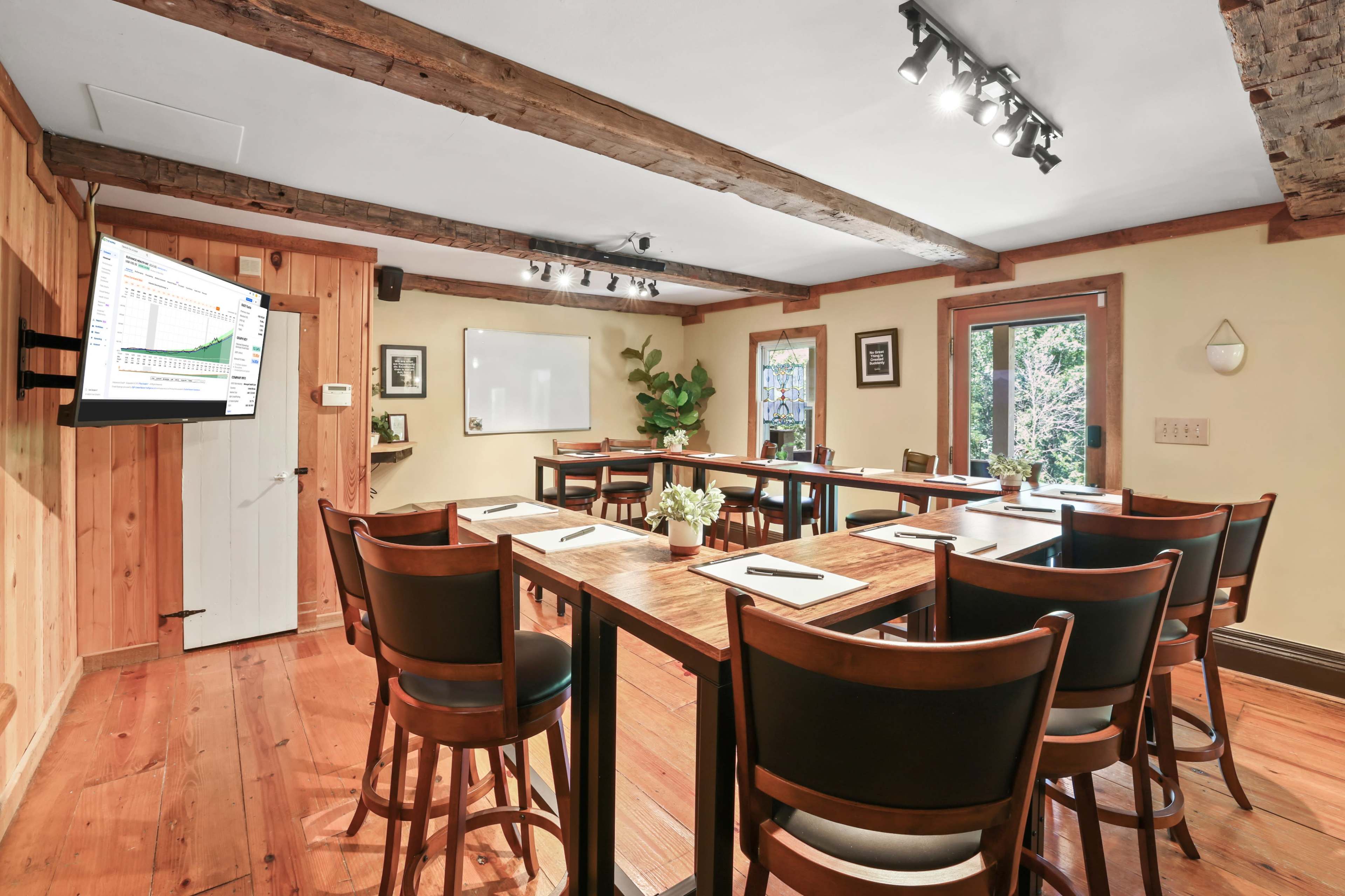 A wood-paneled meeting room features a long table with chairs, a television on the wall, and a sliding door opening to an outdoor view.