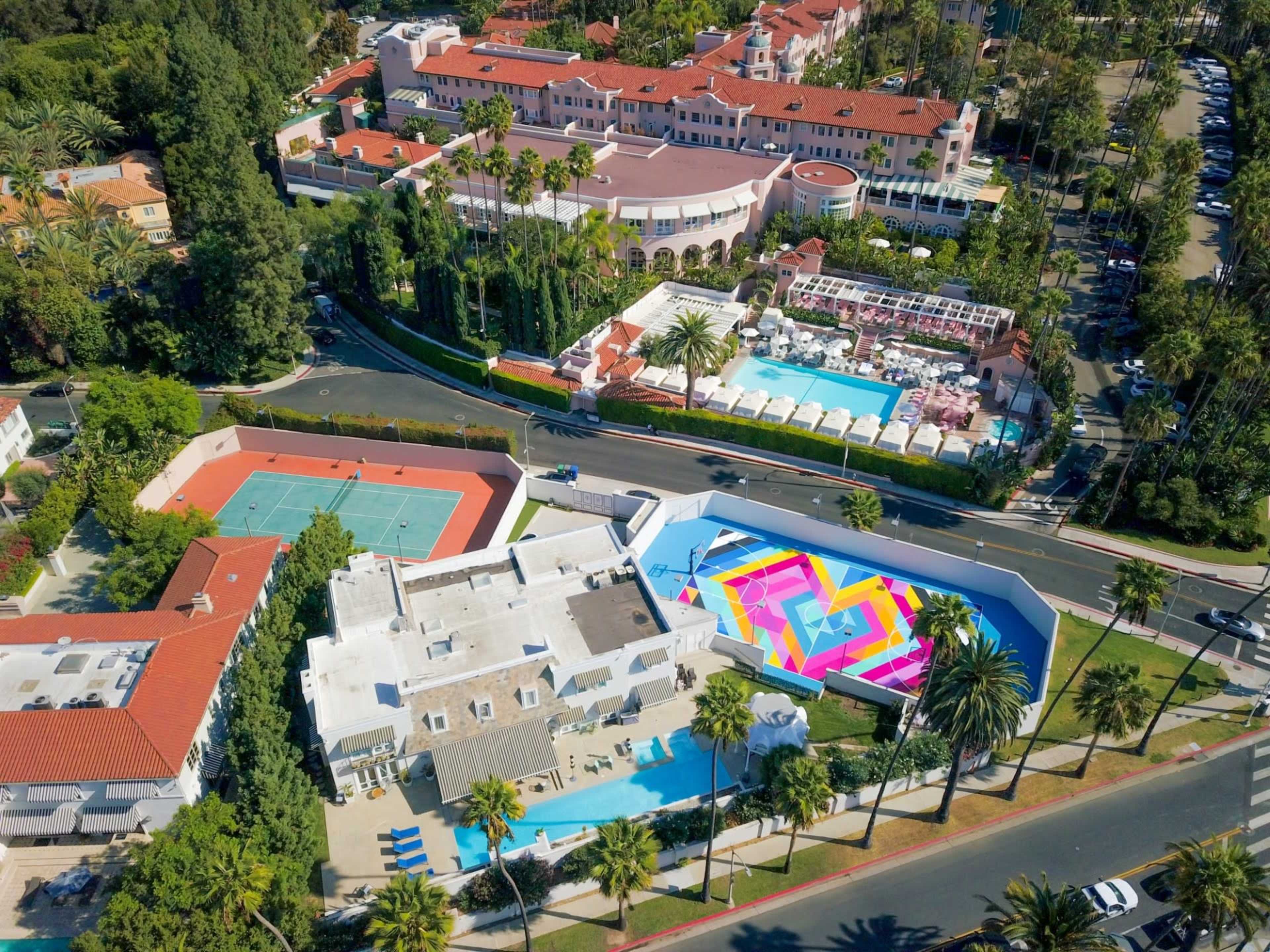 The image shows a resort area featuring multiple swimming pools, tennis courts, and landscaped greenery surrounding the buildings.