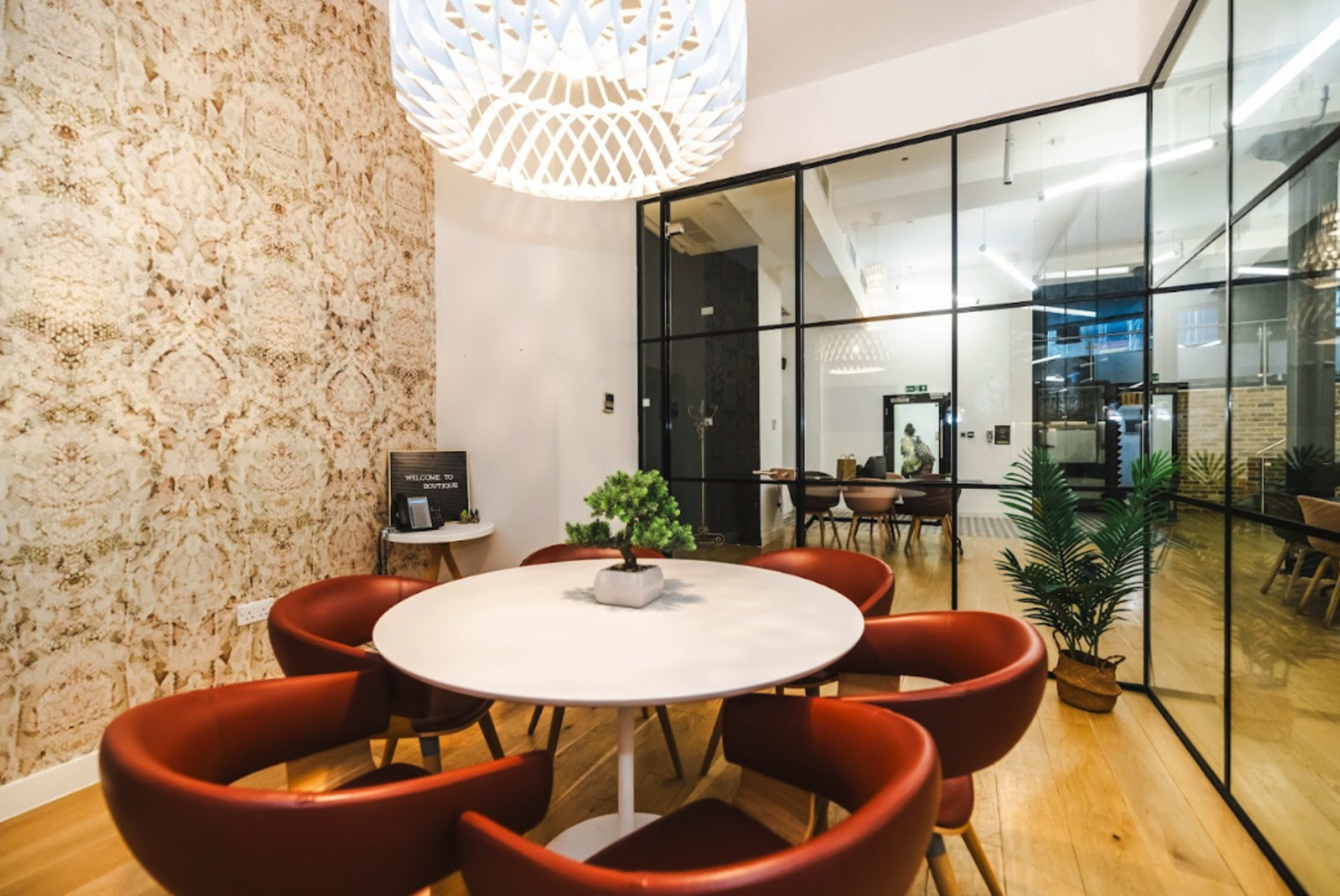 A round table with red chairs is set in a modern room featuring patterned wallpaper and large glass partitions.