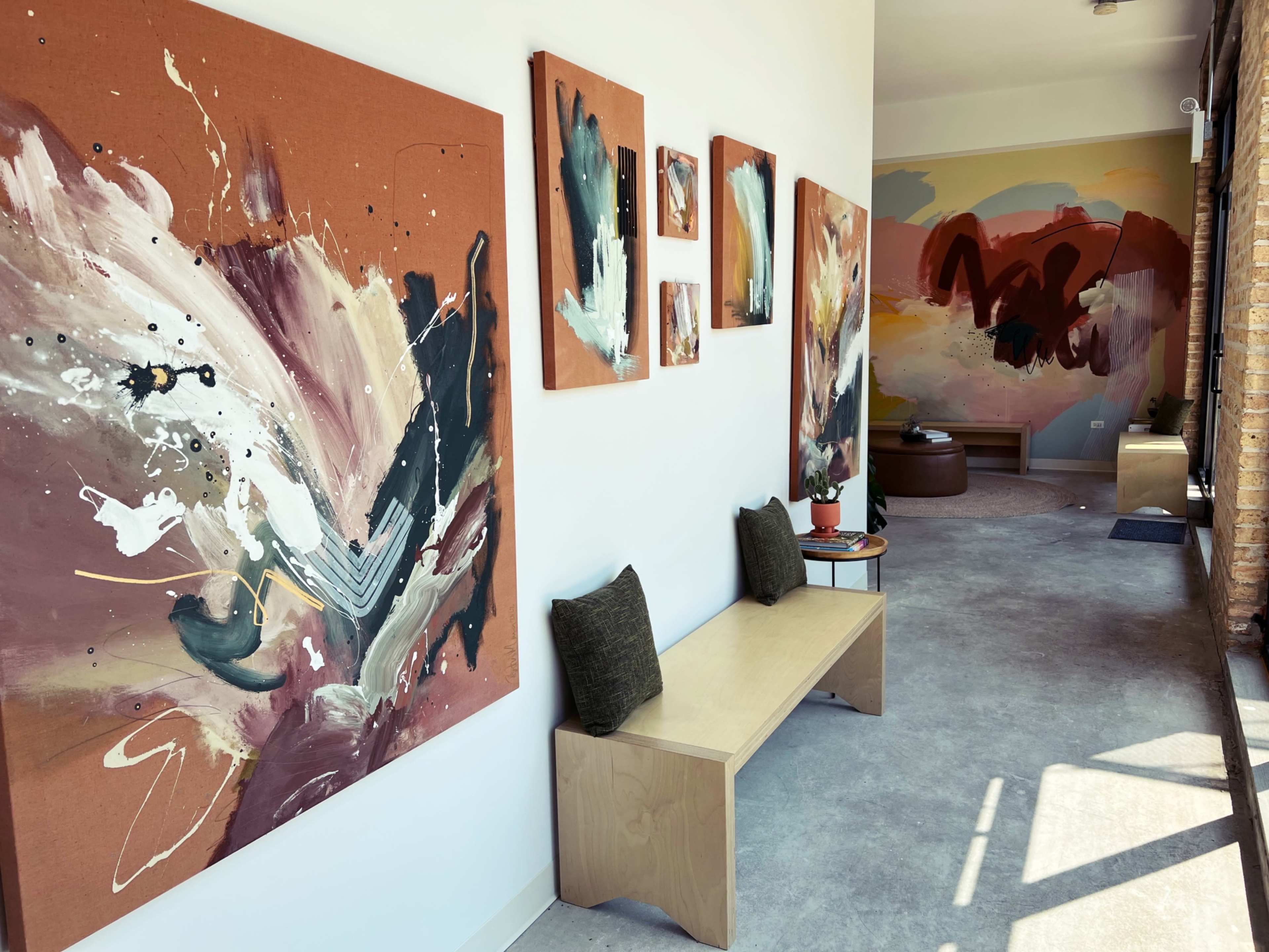 The image shows a hallway with abstract art pieces mounted on the walls and minimalist wooden benches underneath.