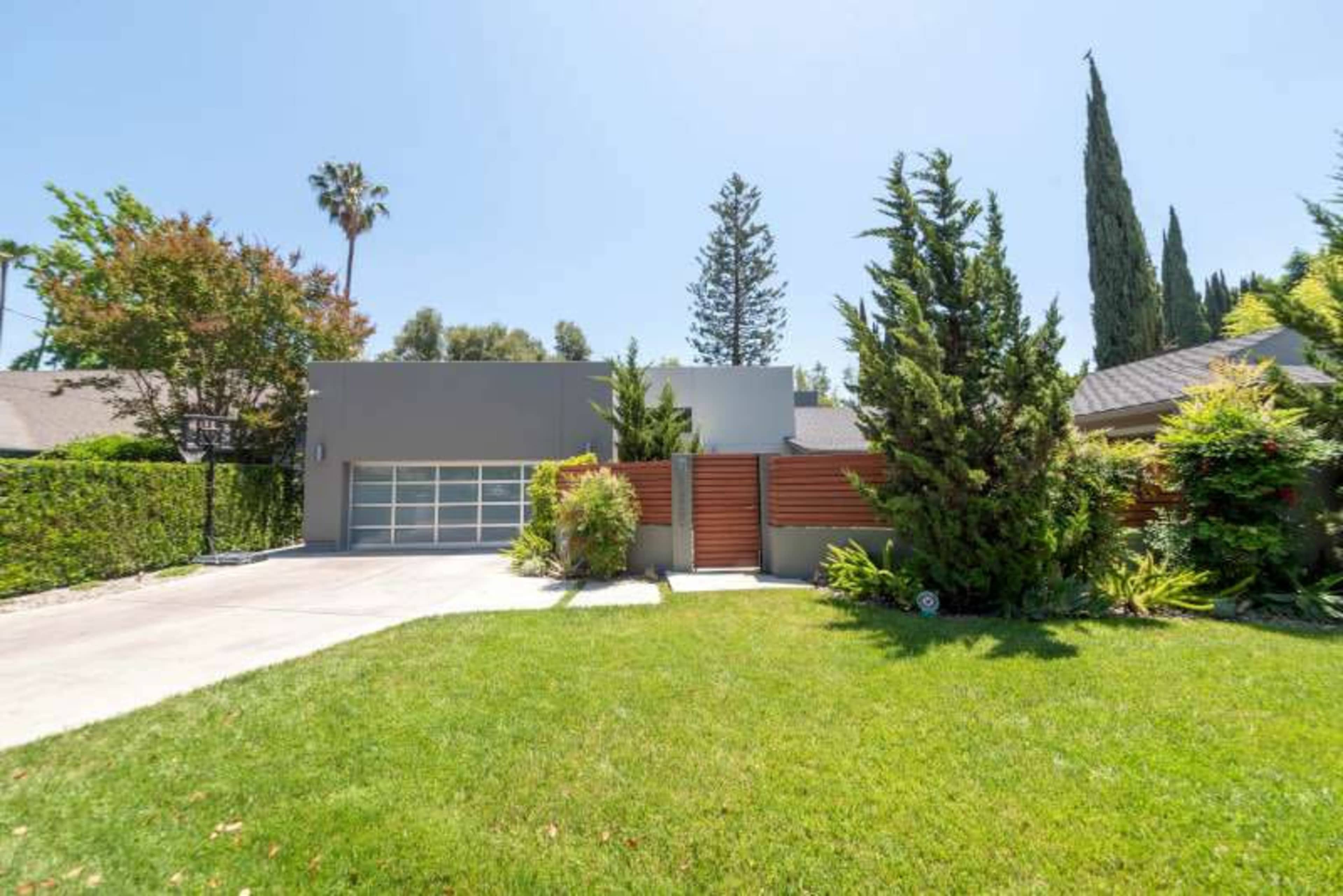 A modern gray house with a two-car garage is set behind a wooden fence and surrounded by well-maintained landscaping.
