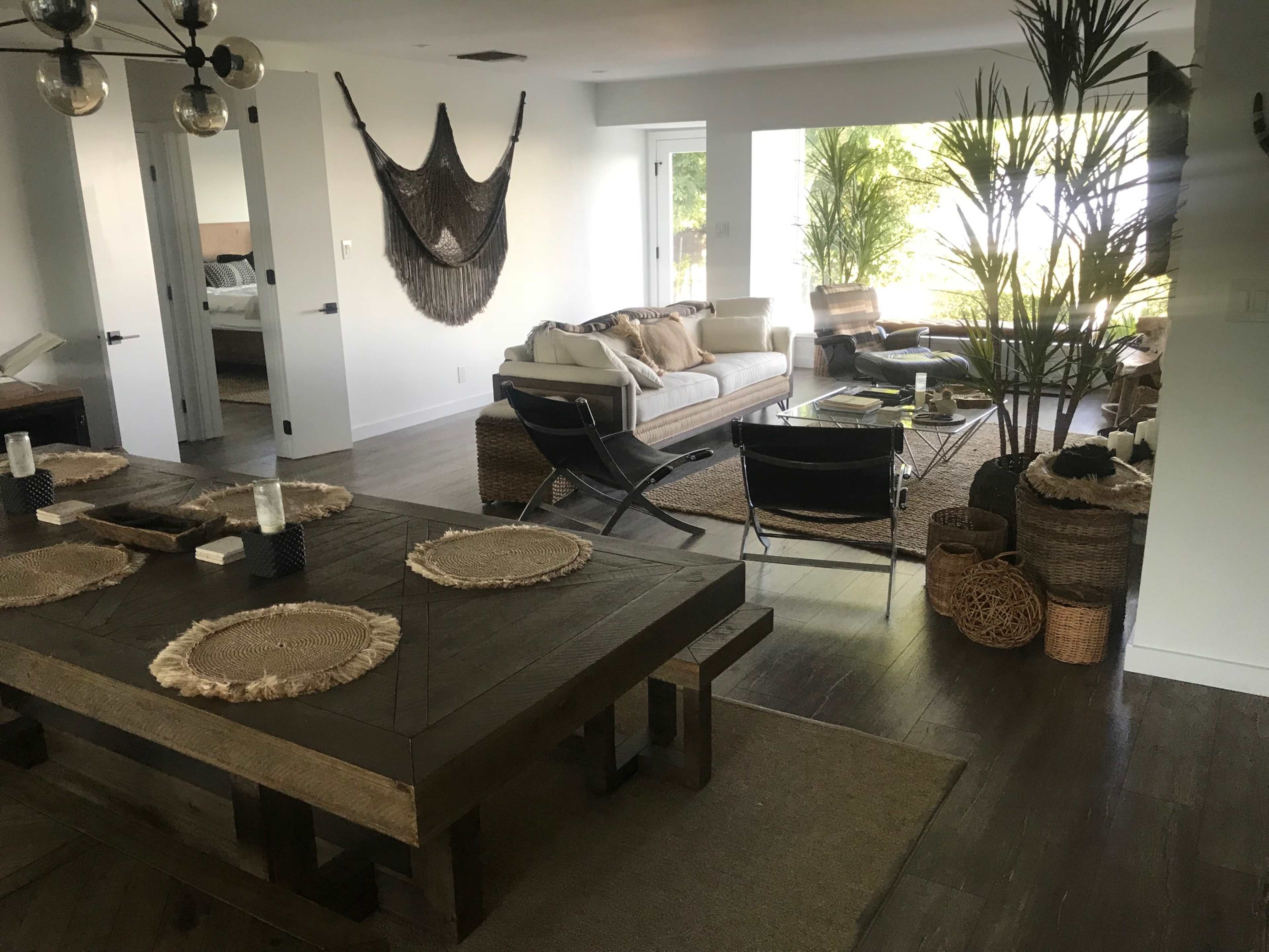 A modern living space with a large wooden dining table, a spacious seating area featuring a sofa, and large windows that let in natural light.
