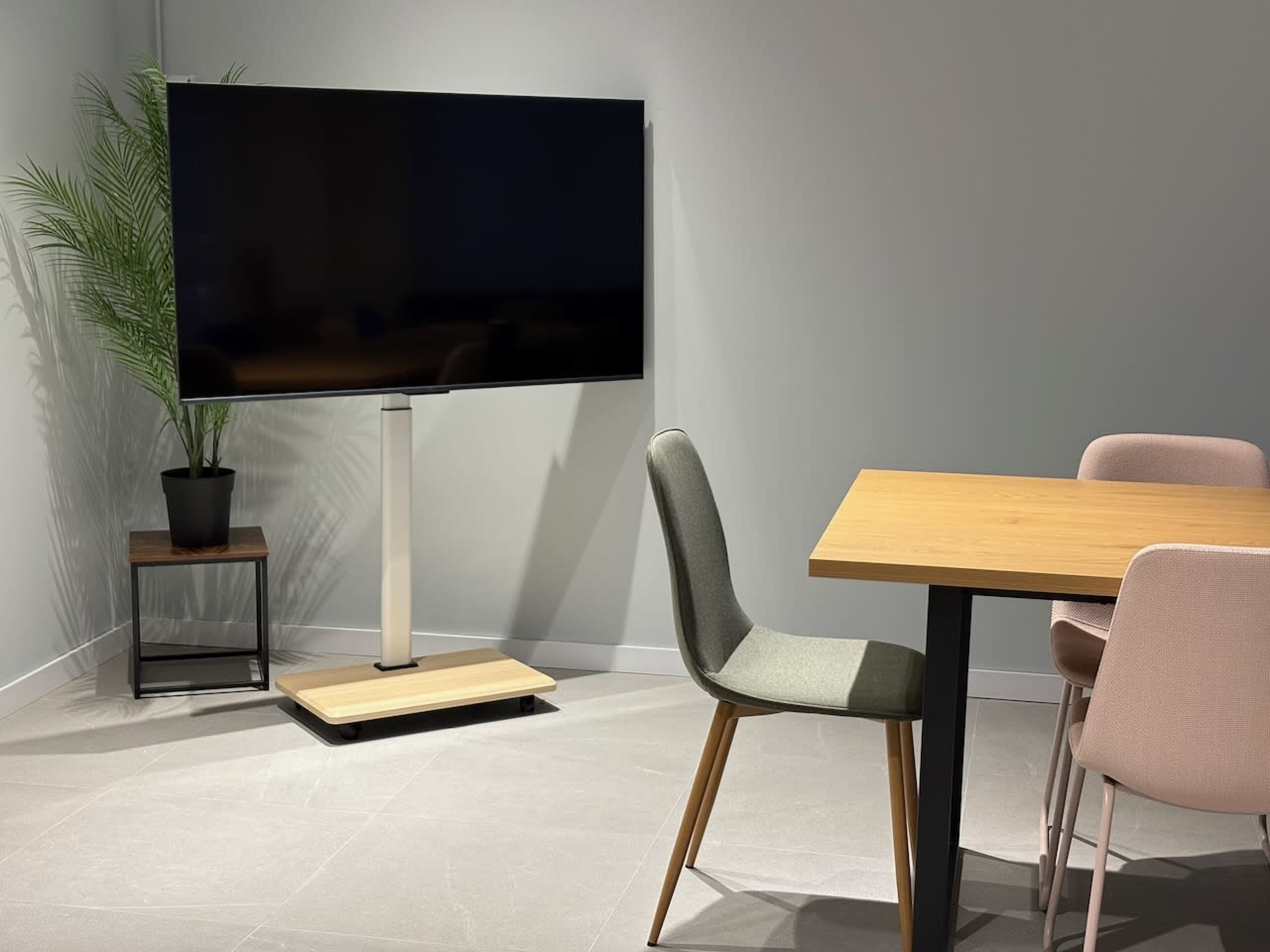 A modern room features a large television mounted on a stand next to a wooden table and three chairs.