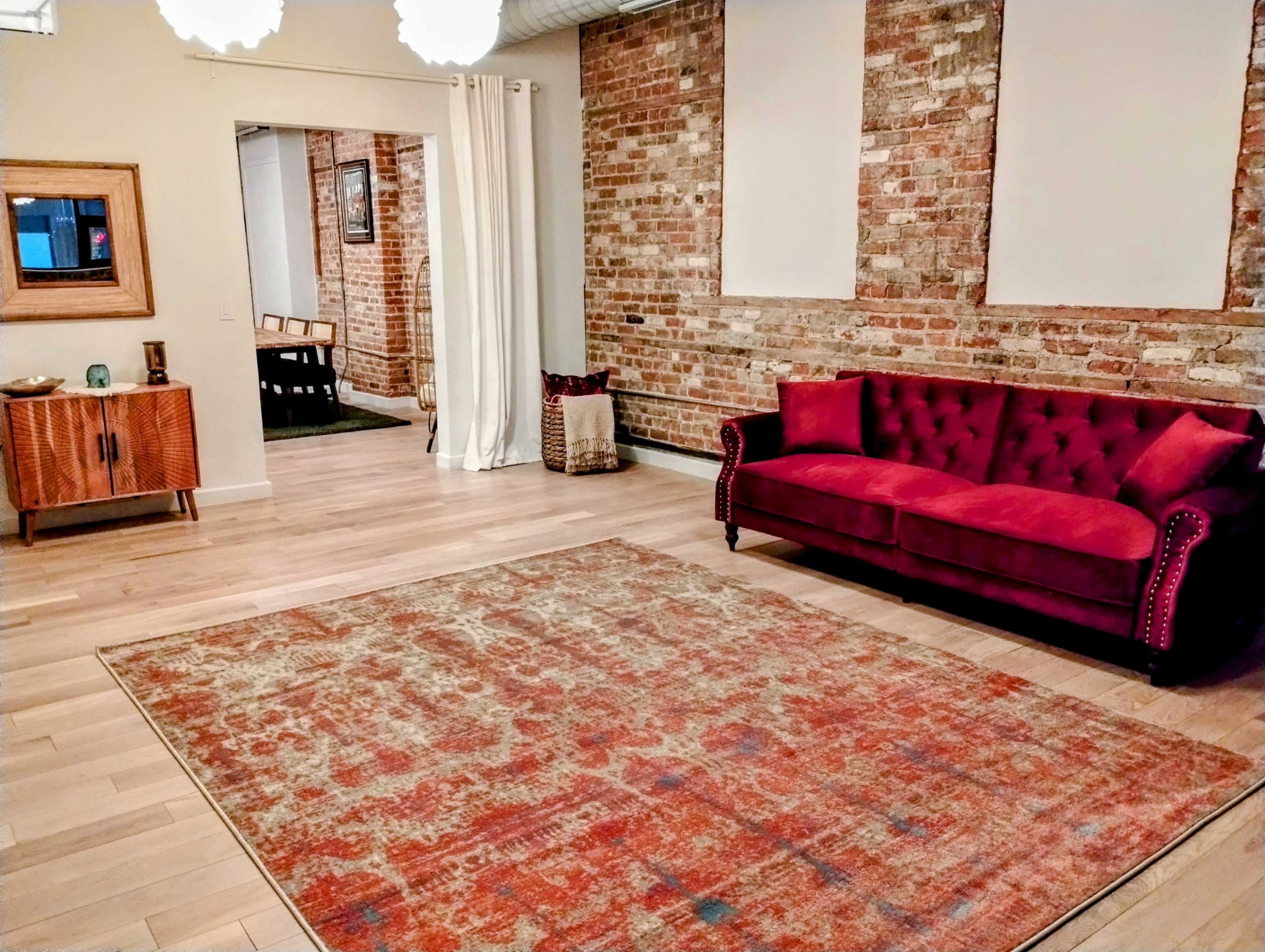 A cozy room with a red tufted sofa, a large area rug, exposed brick walls, and a wooden side table.