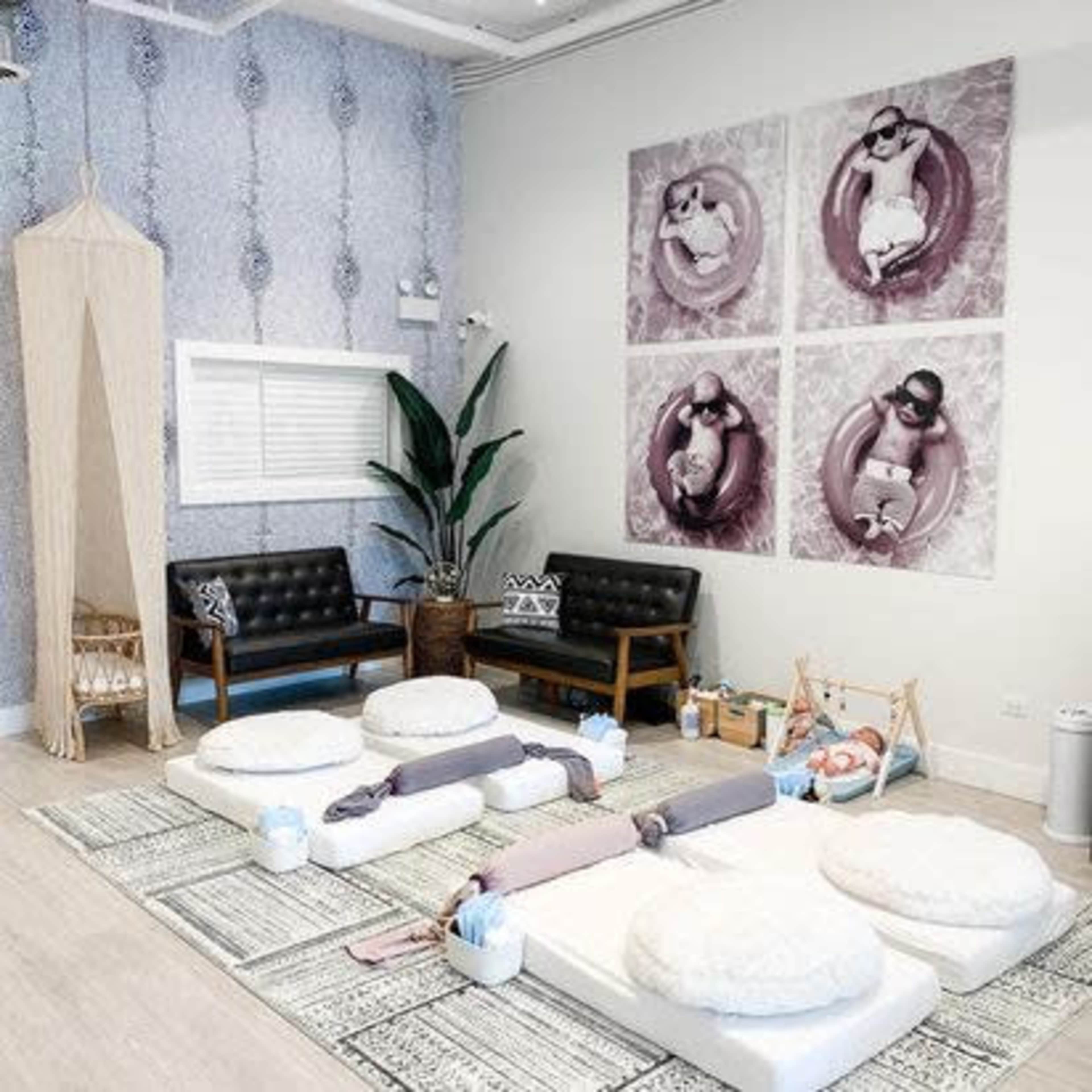 A modern, softly decorated room with circular seating pads, a pair of black sofas, and a large wall display of four photographs featuring people in inflatable rings.