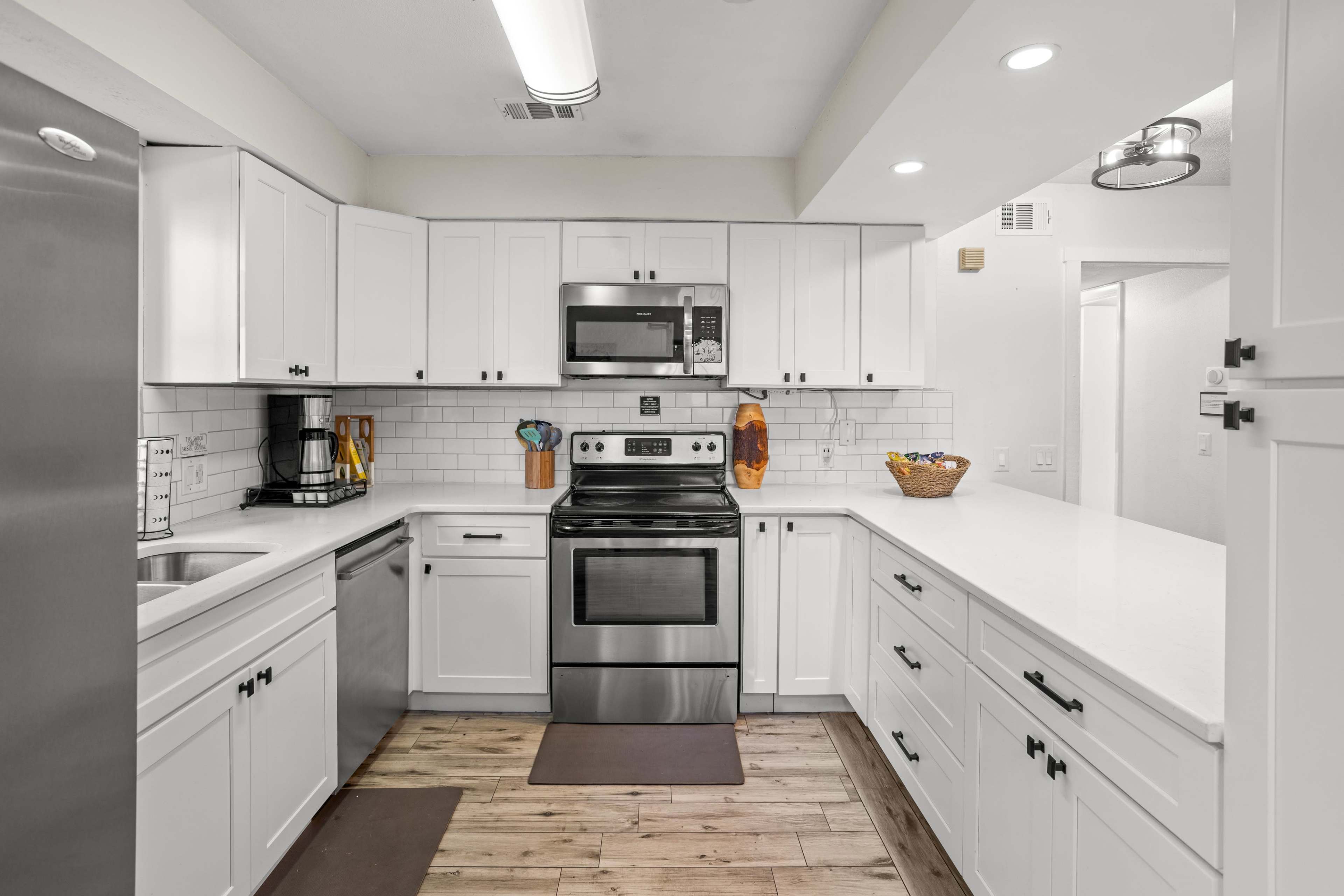 A modern kitchen features white cabinets, stainless steel appliances, and a light wood floor.