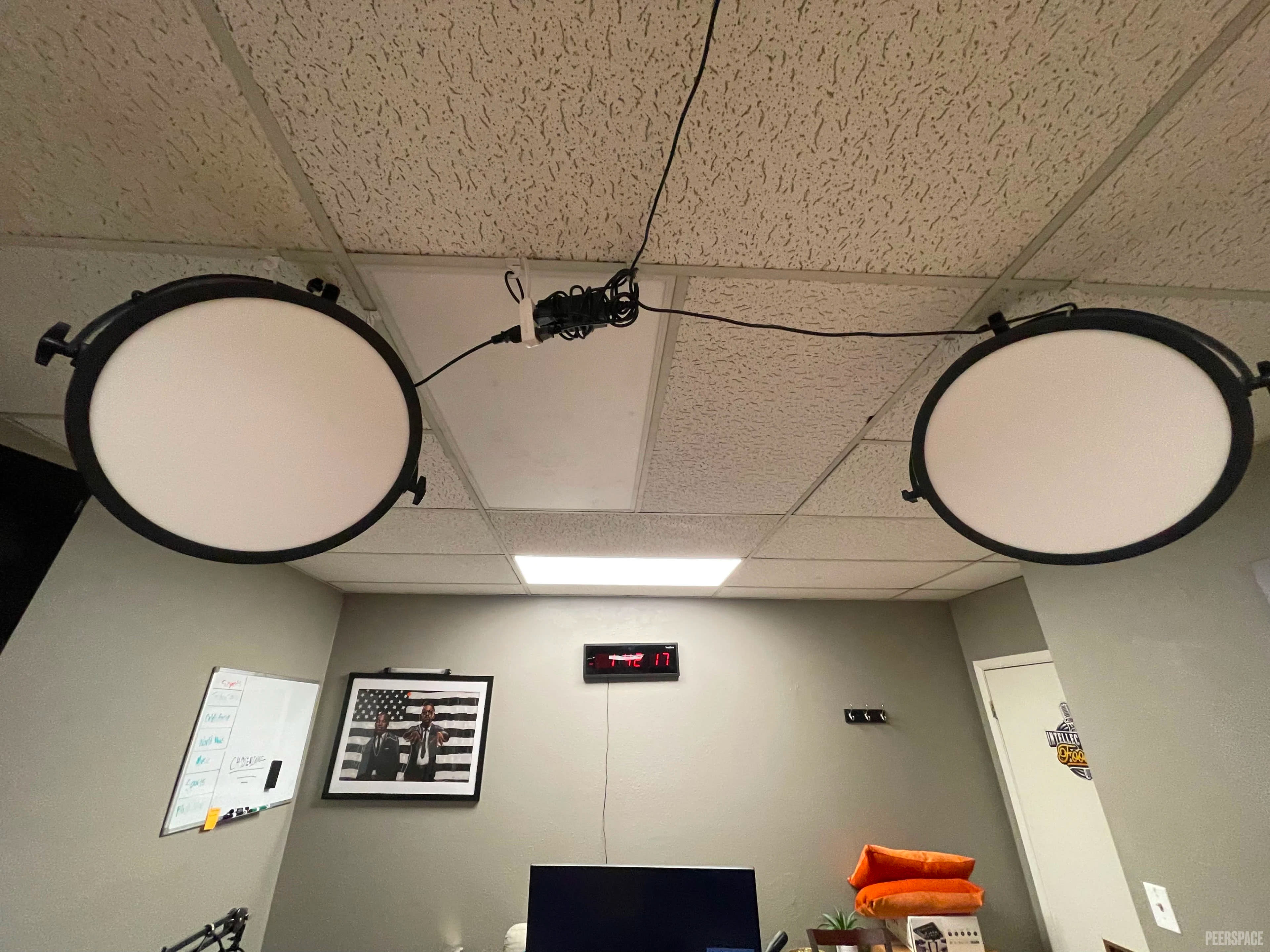 The image shows two circular ceiling lights hanging from the ceiling in a room with gray walls and a whiteboard nearby.