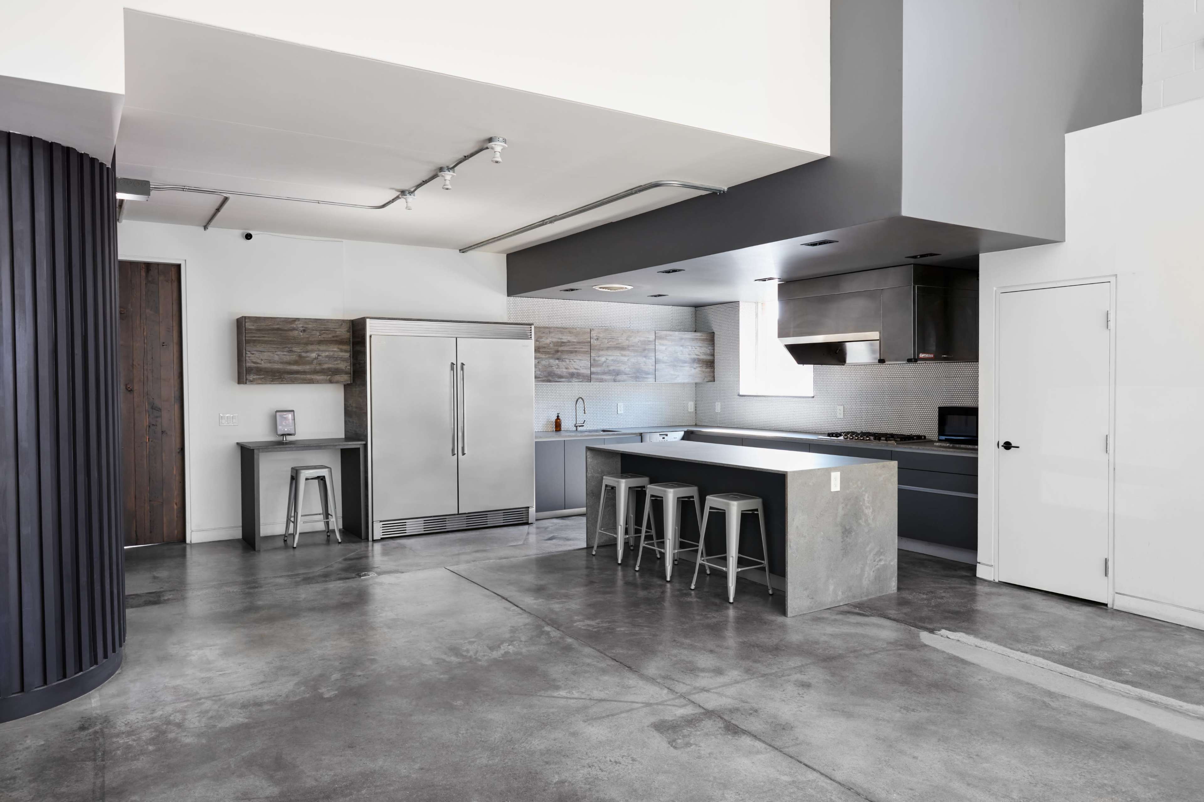 A modern kitchen with stainless steel appliances, concrete flooring, and minimalist cabinetry in a spacious layout.