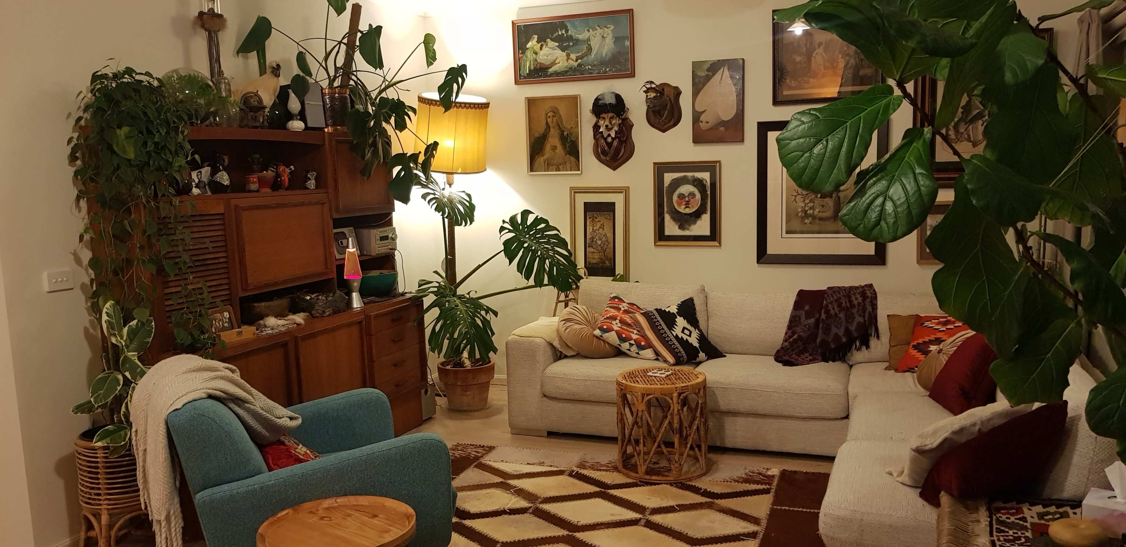 A cozy living room with two sofas, a blue armchair, plants, various wall art, and a wooden side table.