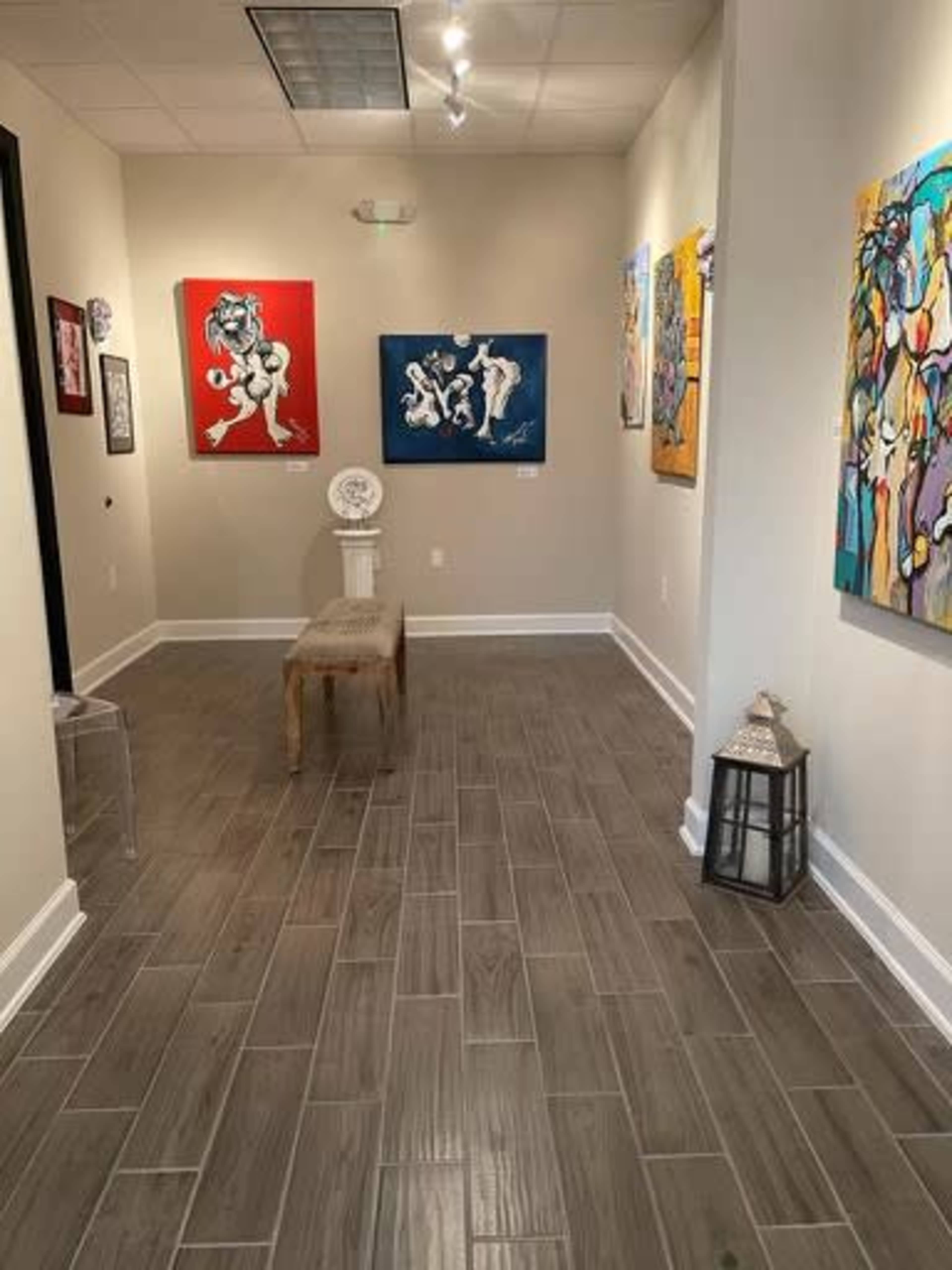 A hallway art gallery with colorful framed paintings displayed on the walls and a wooden bench along the floor.