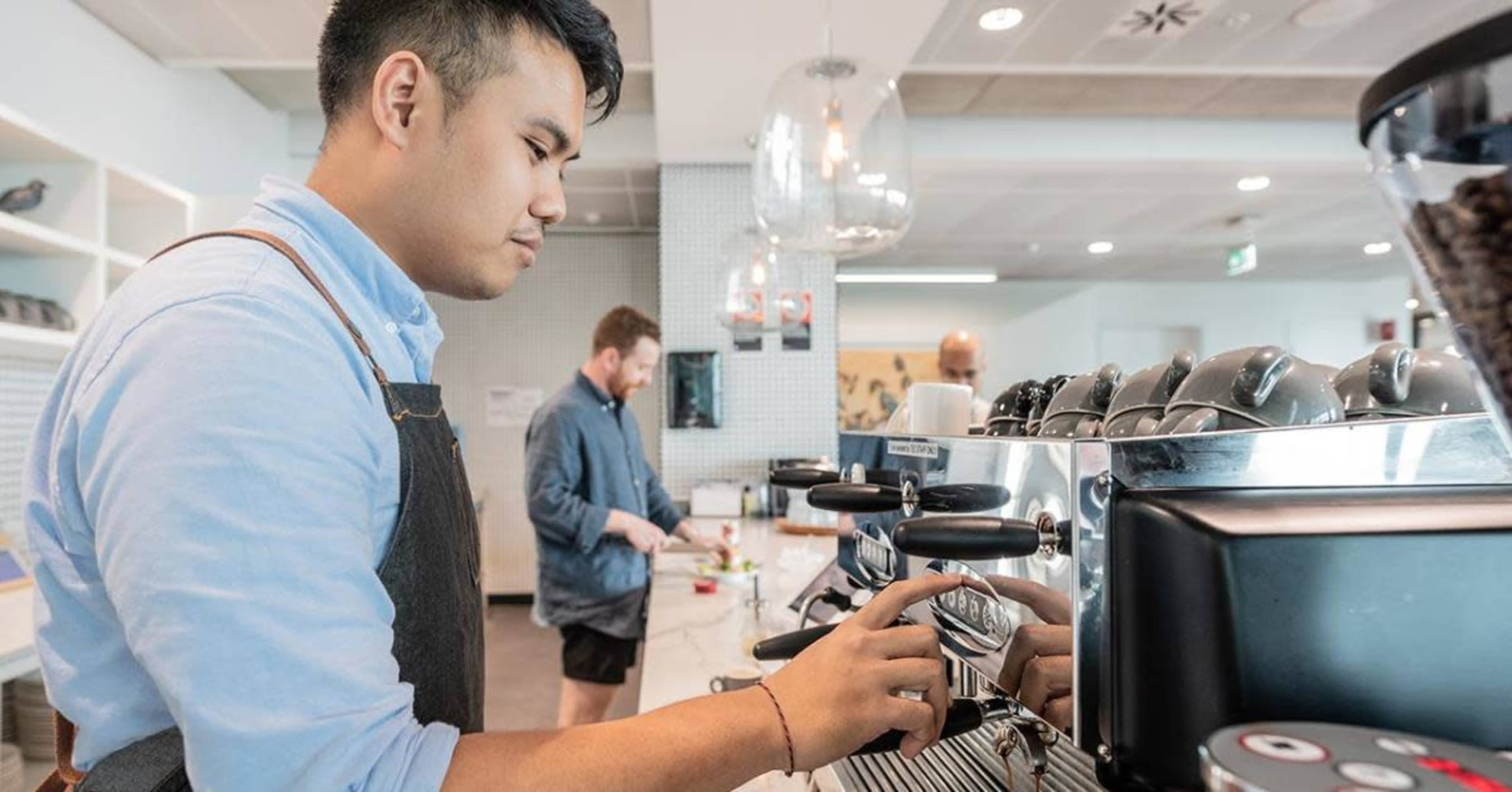 A barista operates an espresso machine while another man prepares coffee in a modern café.