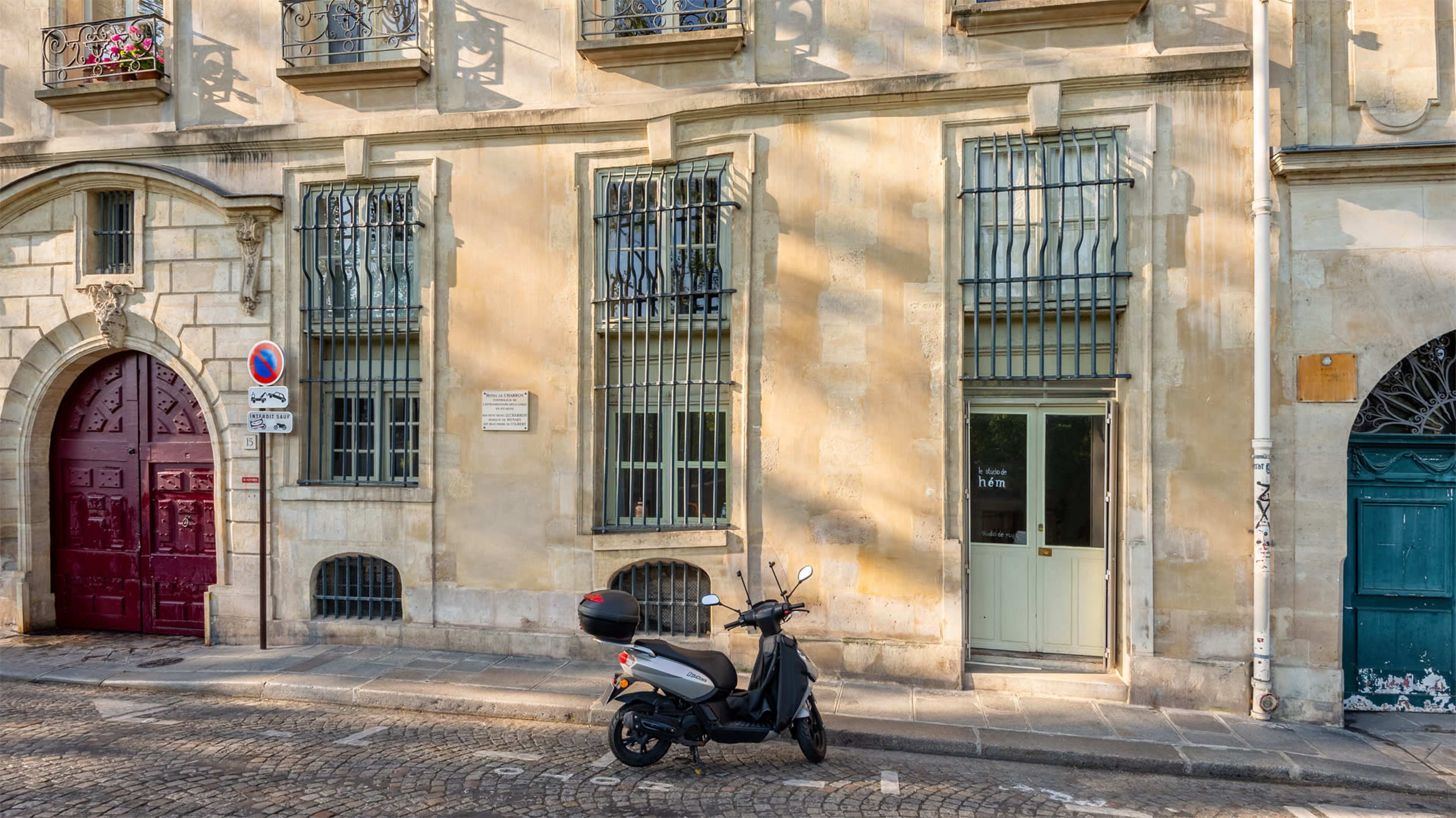 A scooter is parked on a cobblestone street in front of a building with multiple windows and decorative iron bars.