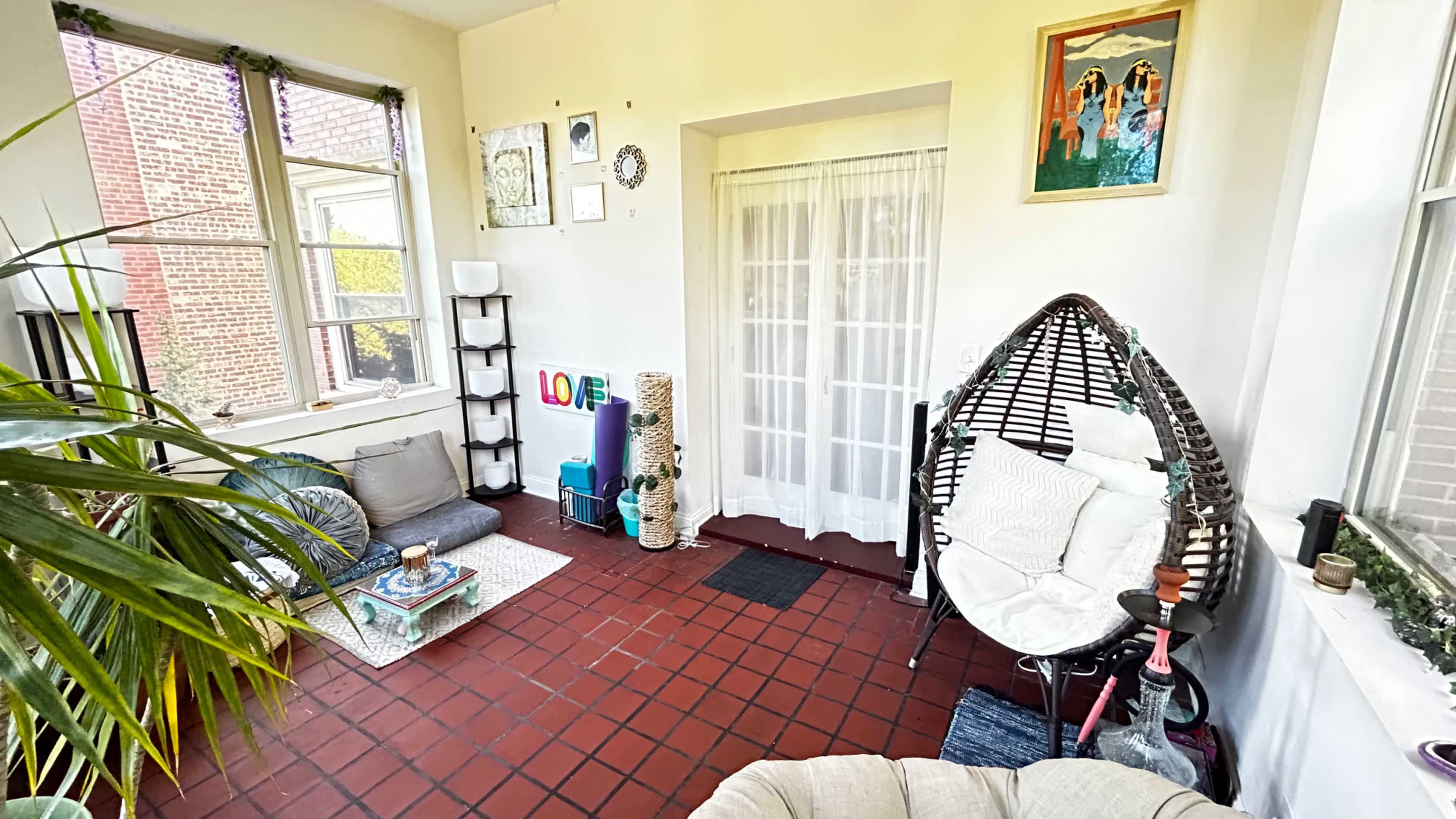 The image shows a cozy indoor space with a hanging chair, a small coffee table, and colorful decorations on the walls.