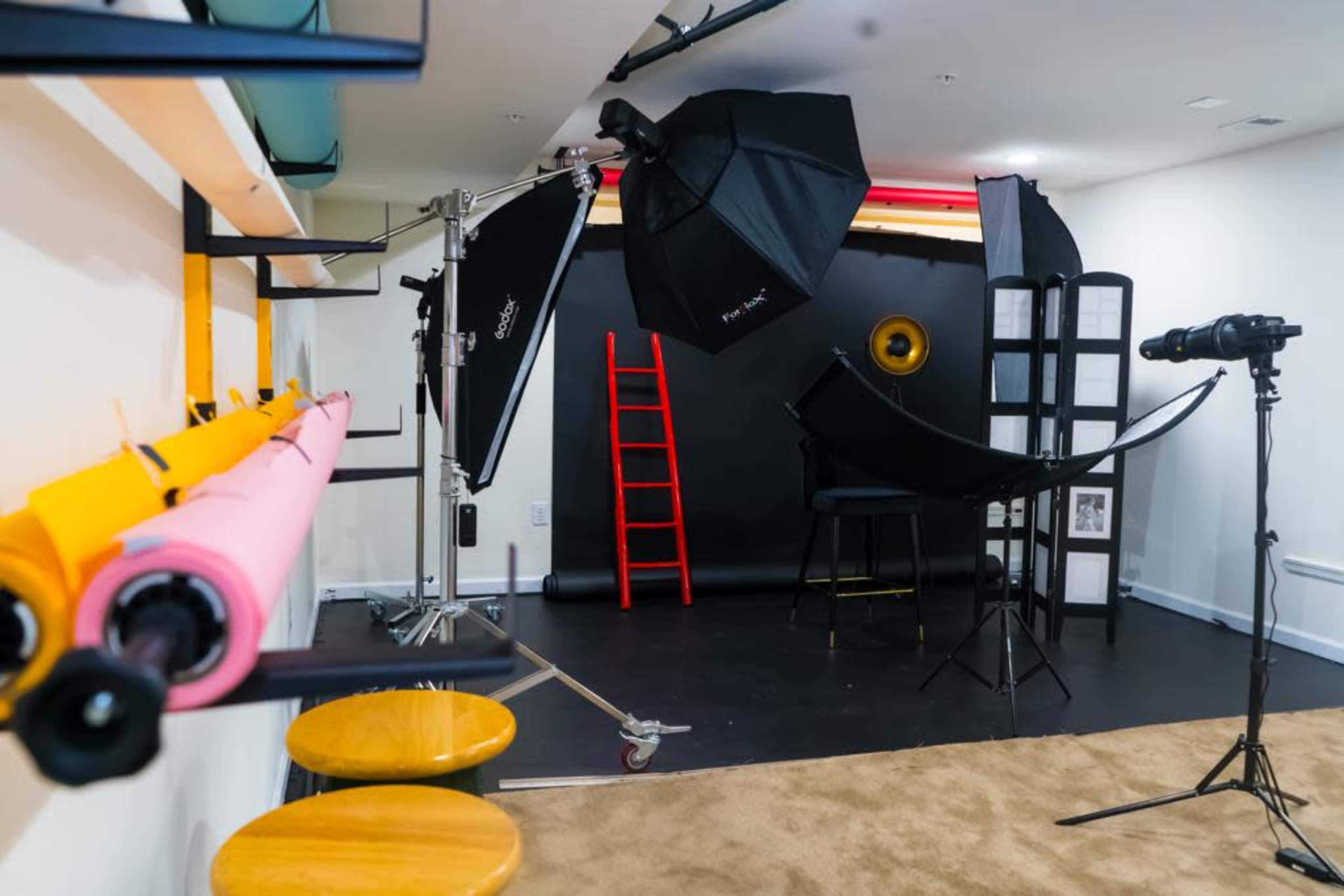 A photography studio setup, featuring backdrops, lighting equipment, a ladder, and a camera on a tripod.