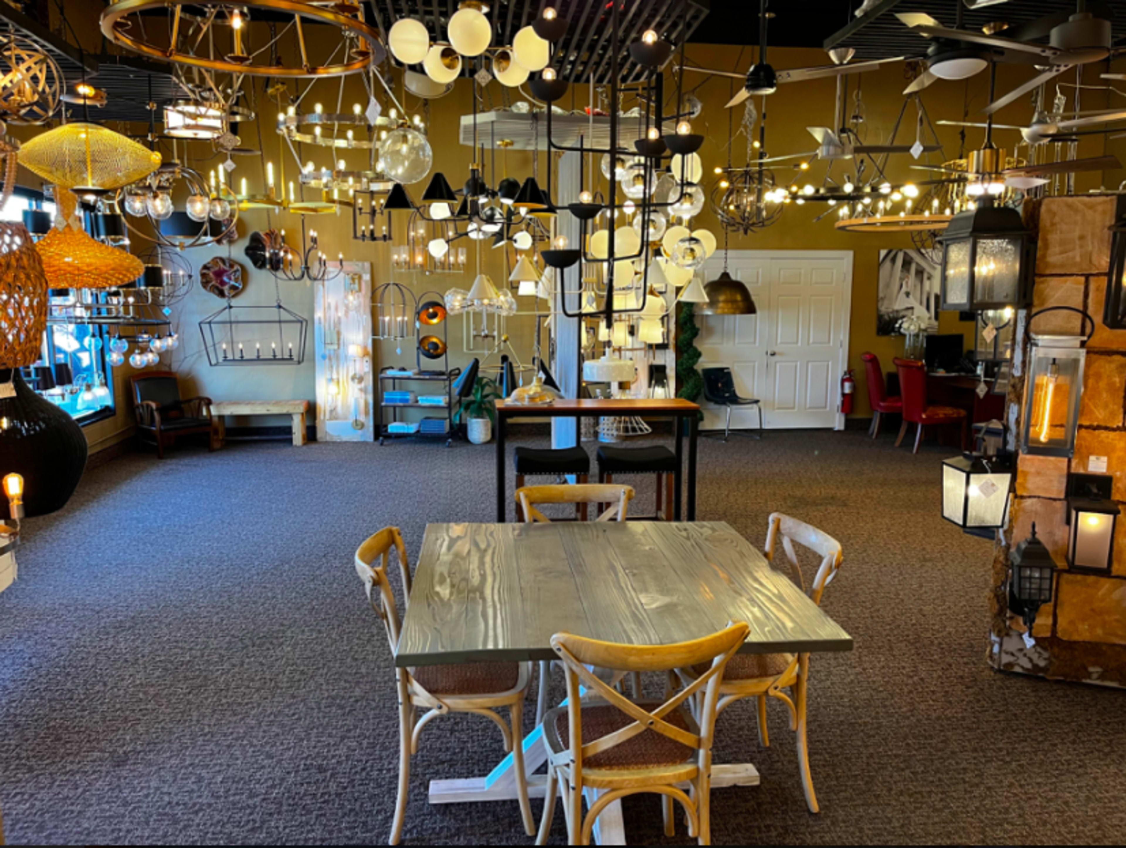 A showroom filled with various lighting fixtures and furniture, featuring a central table surrounded by chairs.