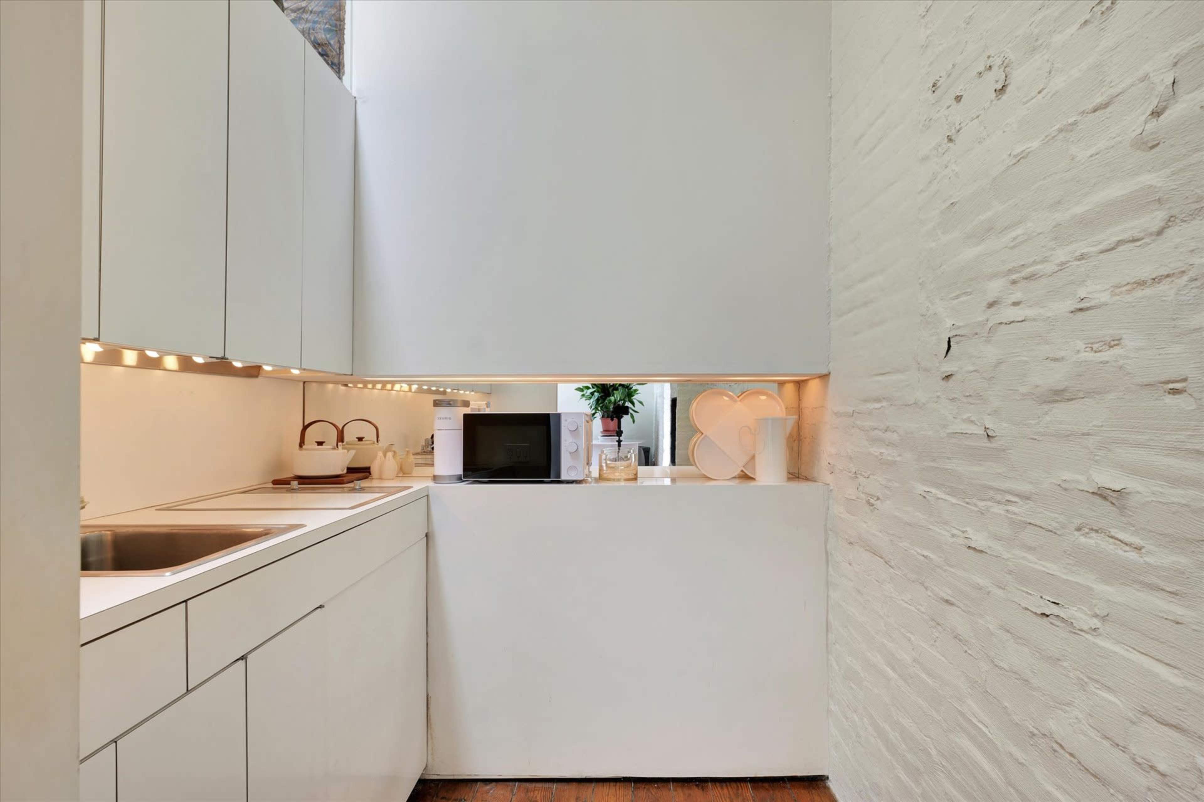 A modern kitchen with white cabinetry, a stainless steel sink, and a microwave positioned on a countertop.