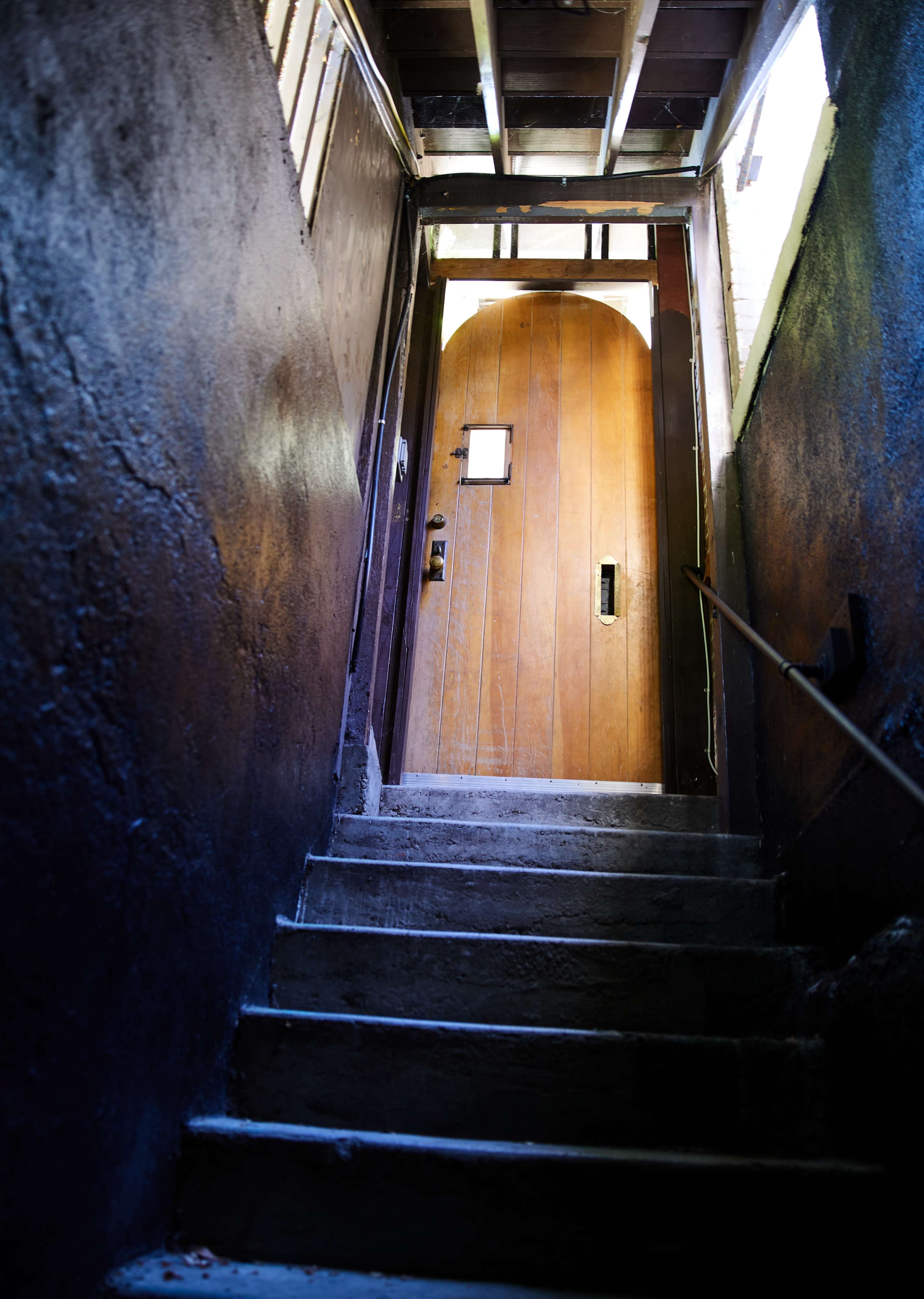 A wooden door stands at the top of a narrow staircase, illuminated by natural light.