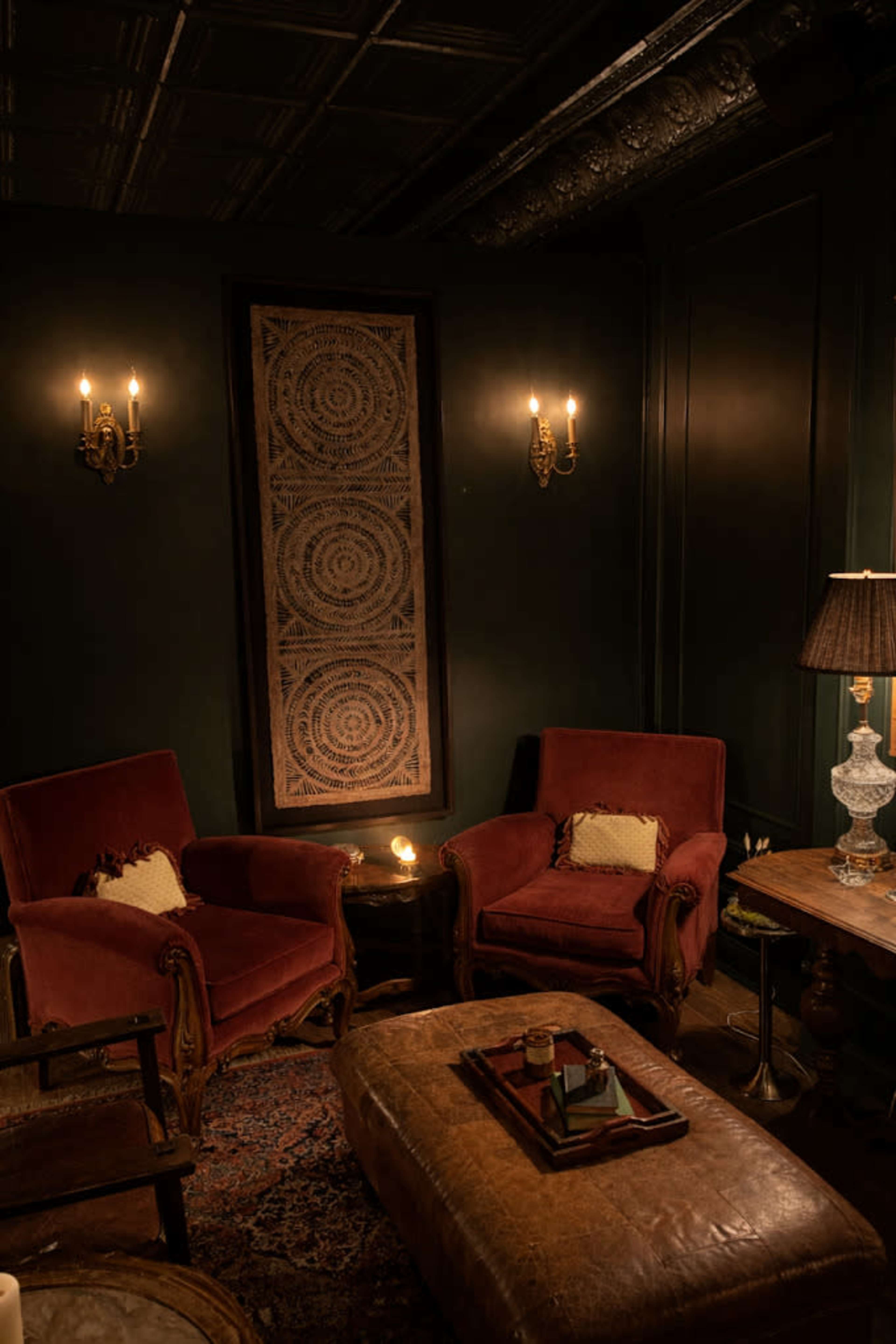 The image showcases a cozy sitting area with two red armchairs, a wooden table, and soft lighting from wall sconces and a lamp.