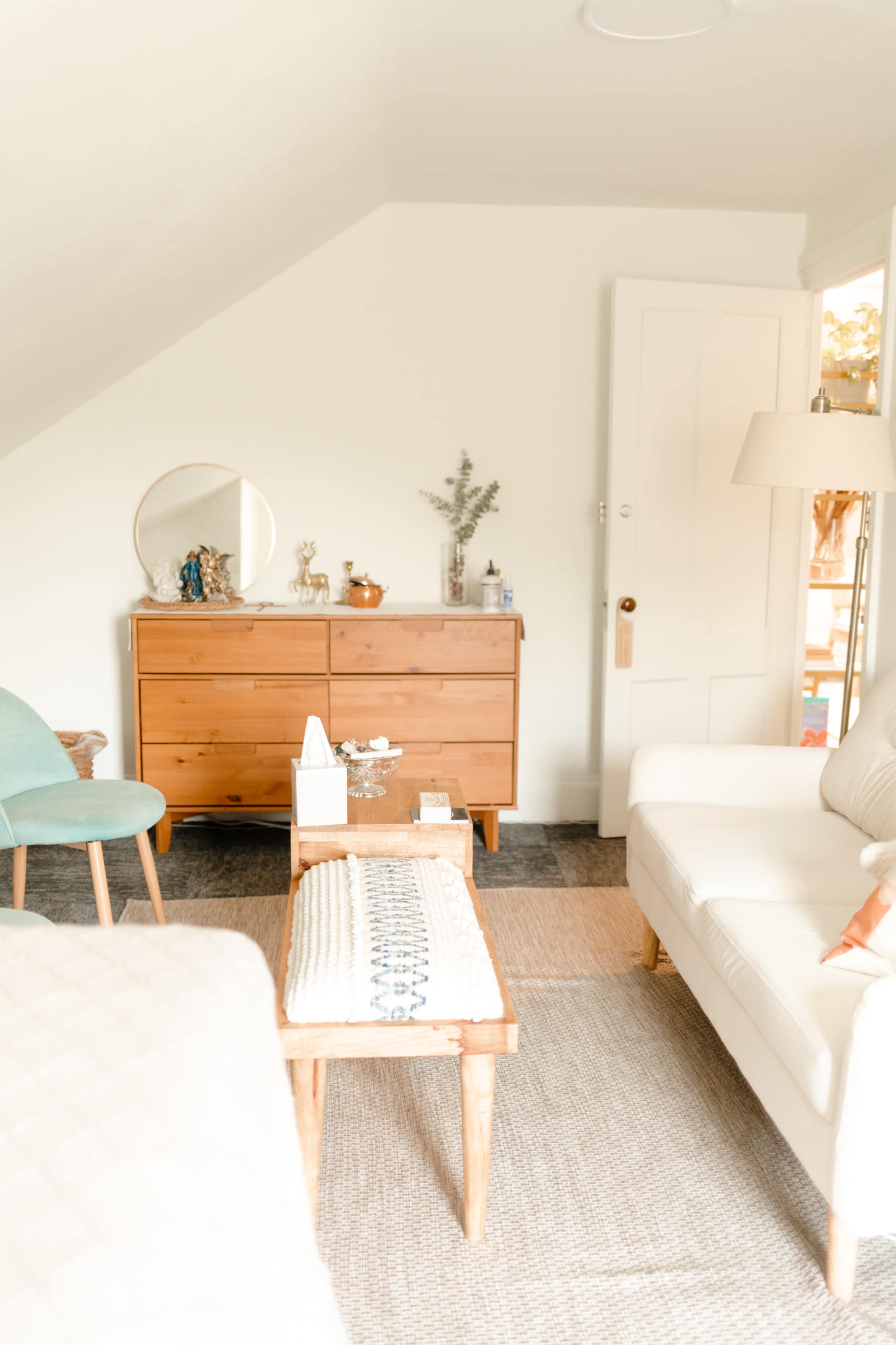 A cozy room with a wooden dresser, a light-colored sofa, a small table, and a blue accent chair.