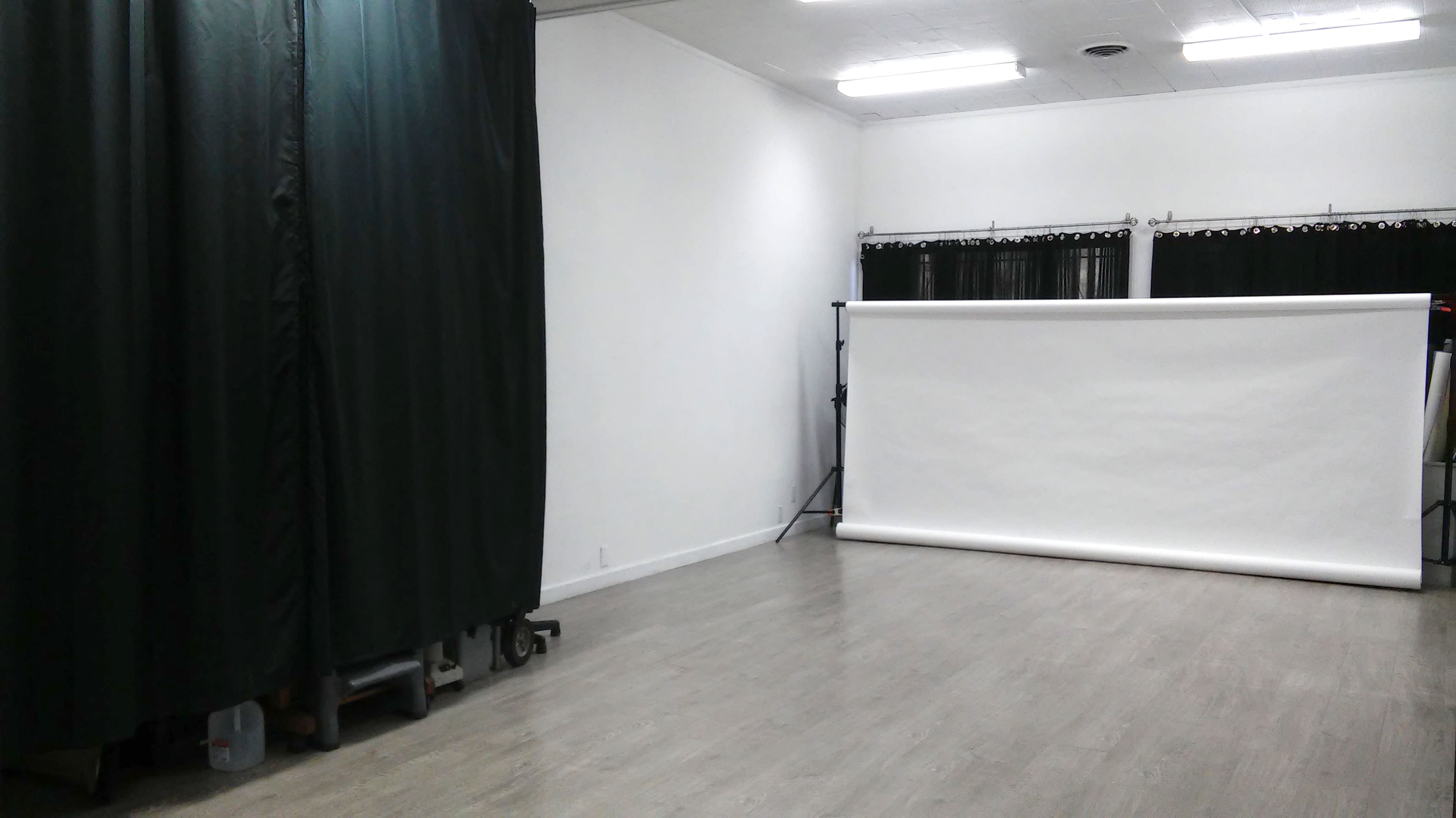 A spacious room with a clean floor, featuring a white backdrop on stands and dark curtains along one side.