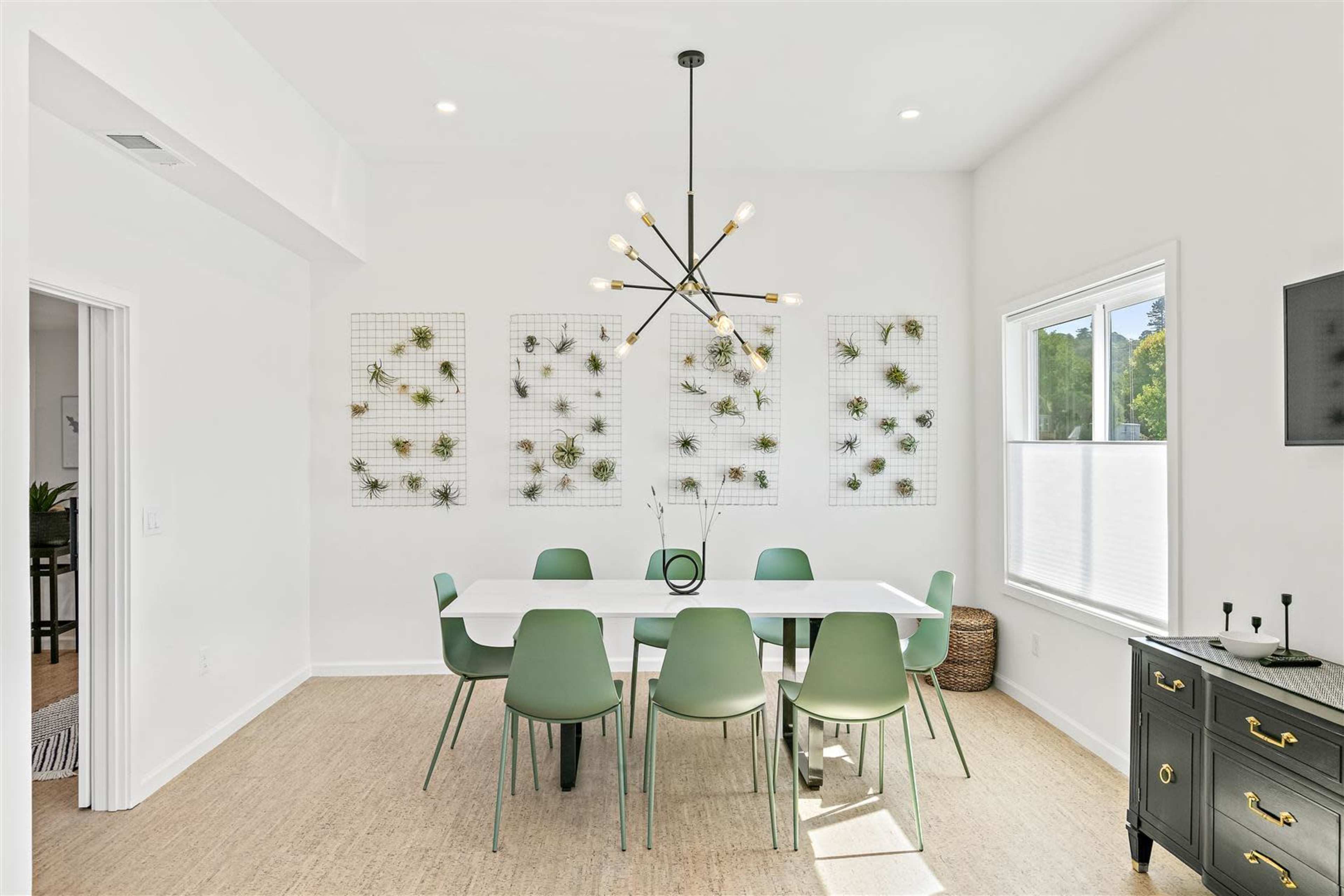 A modern dining area features a white table surrounded by green chairs, with wall-mounted plant displays and a stylish light fixture overhead.