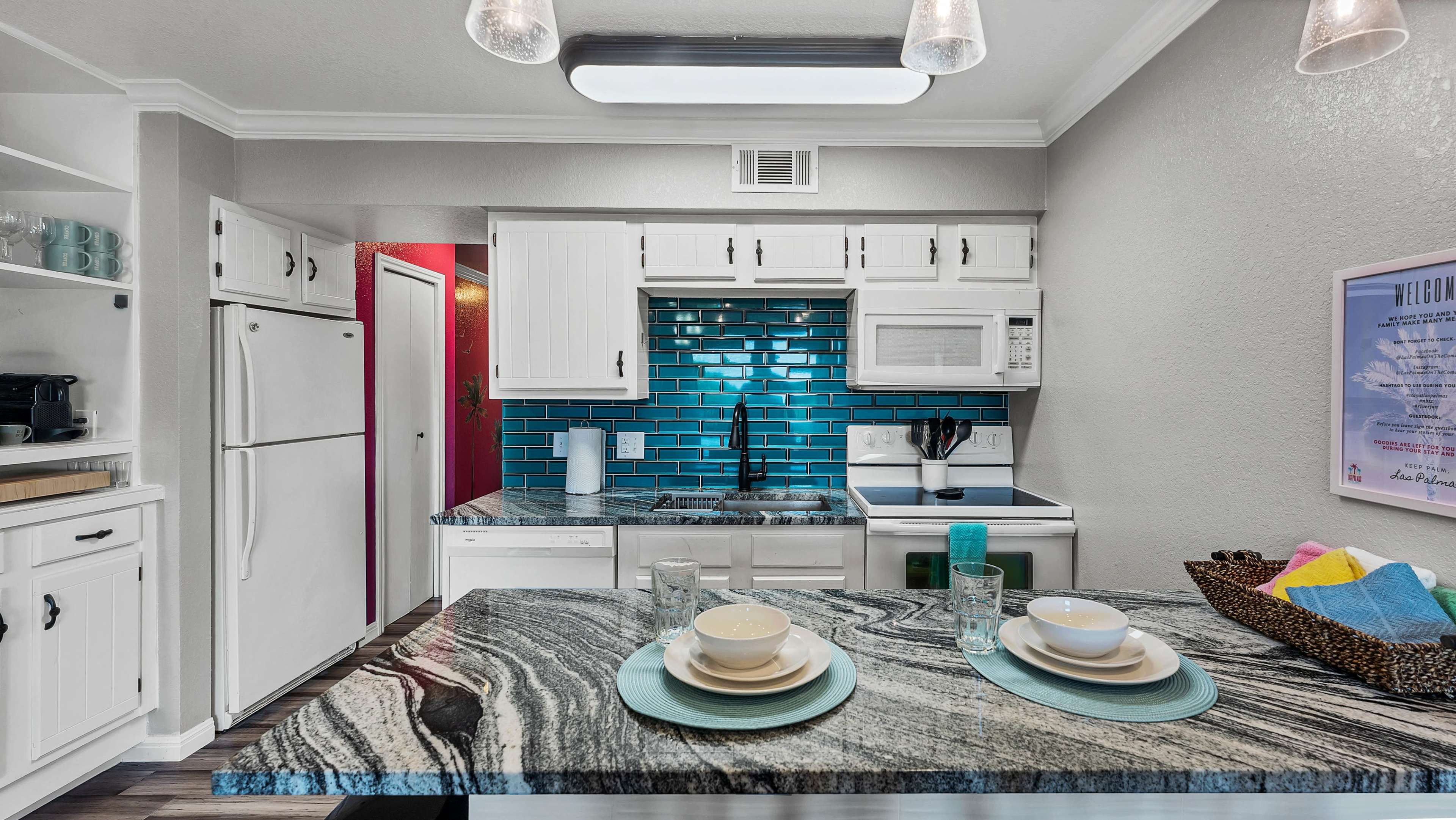 A modern kitchen features white cabinets, a teal tiled backsplash, and a granite countertop with place settings.