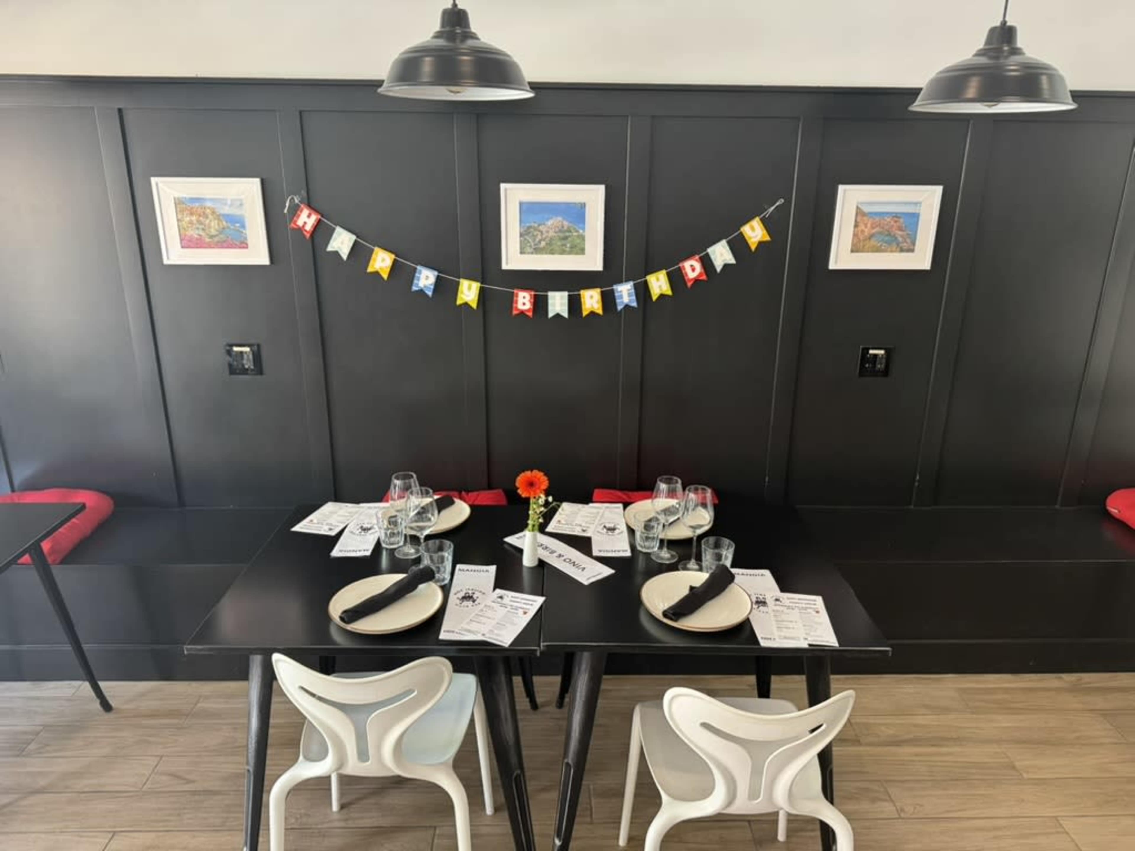 A black-walled dining area features a table set for a birthday celebration, adorned with a colorful "Happy Birthday" banner and floral centerpiece.