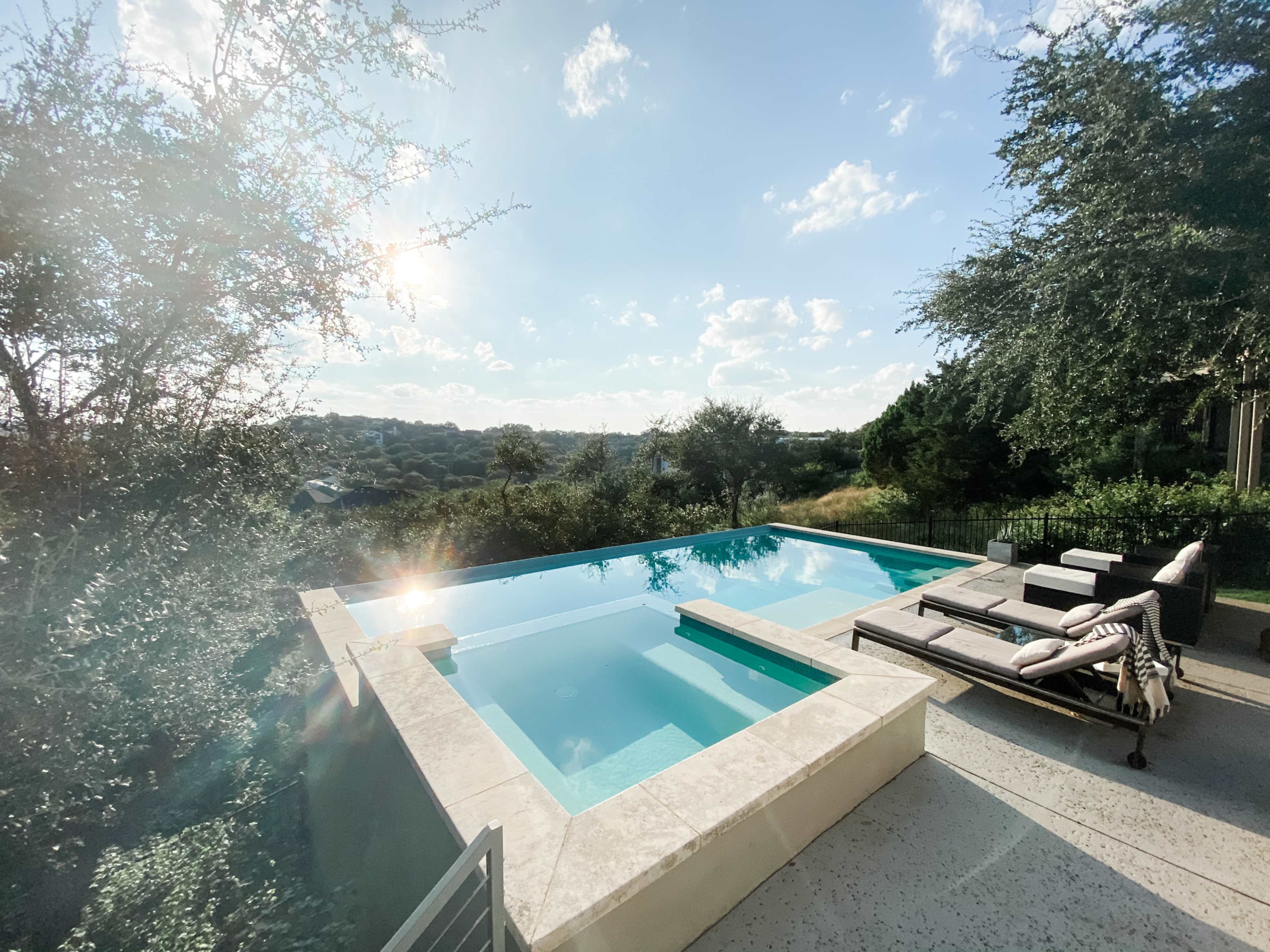 A modern infinity pool overlooking a green landscape under a partly cloudy sky.