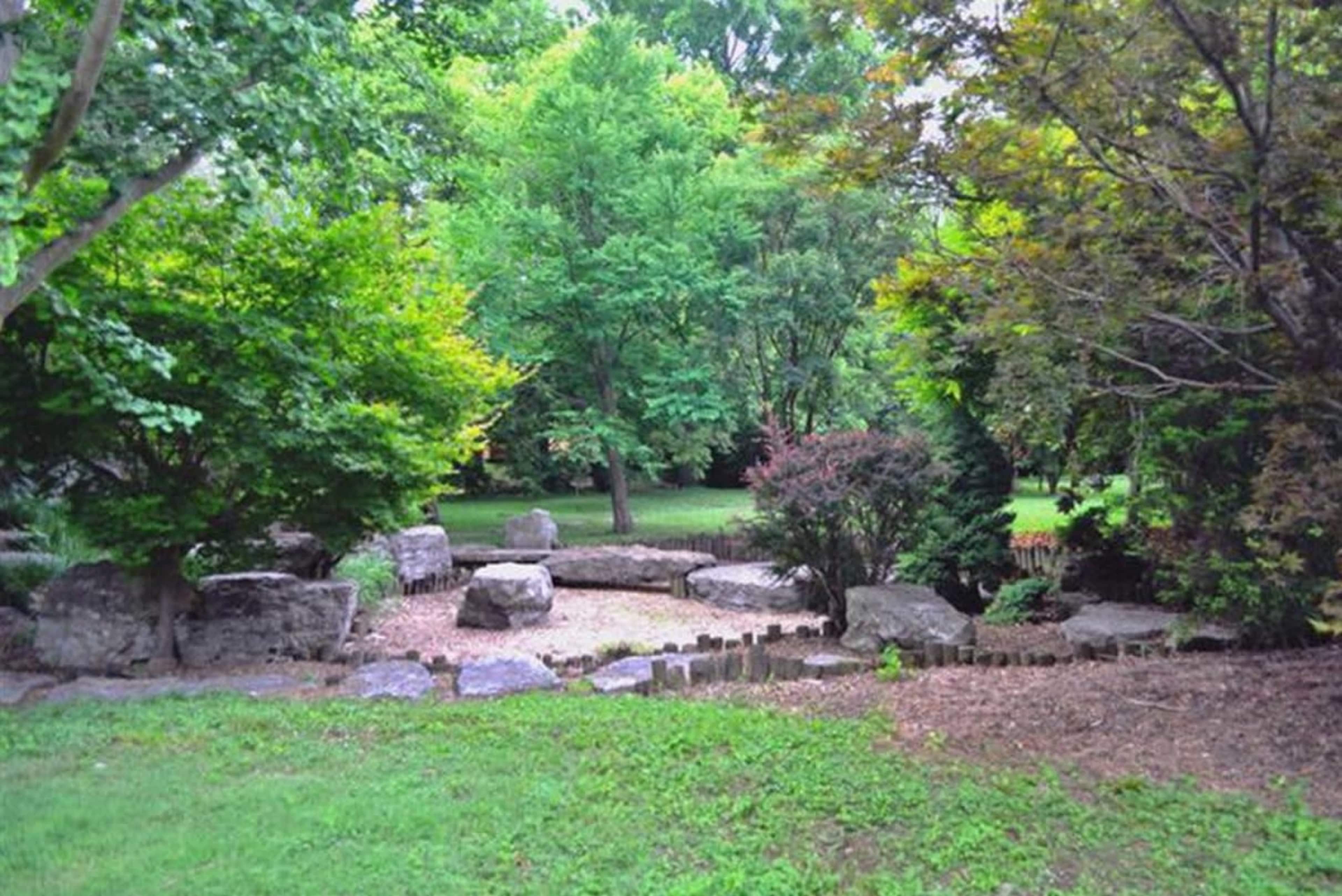 A serene garden features a clearing surrounded by trees and large rocks.