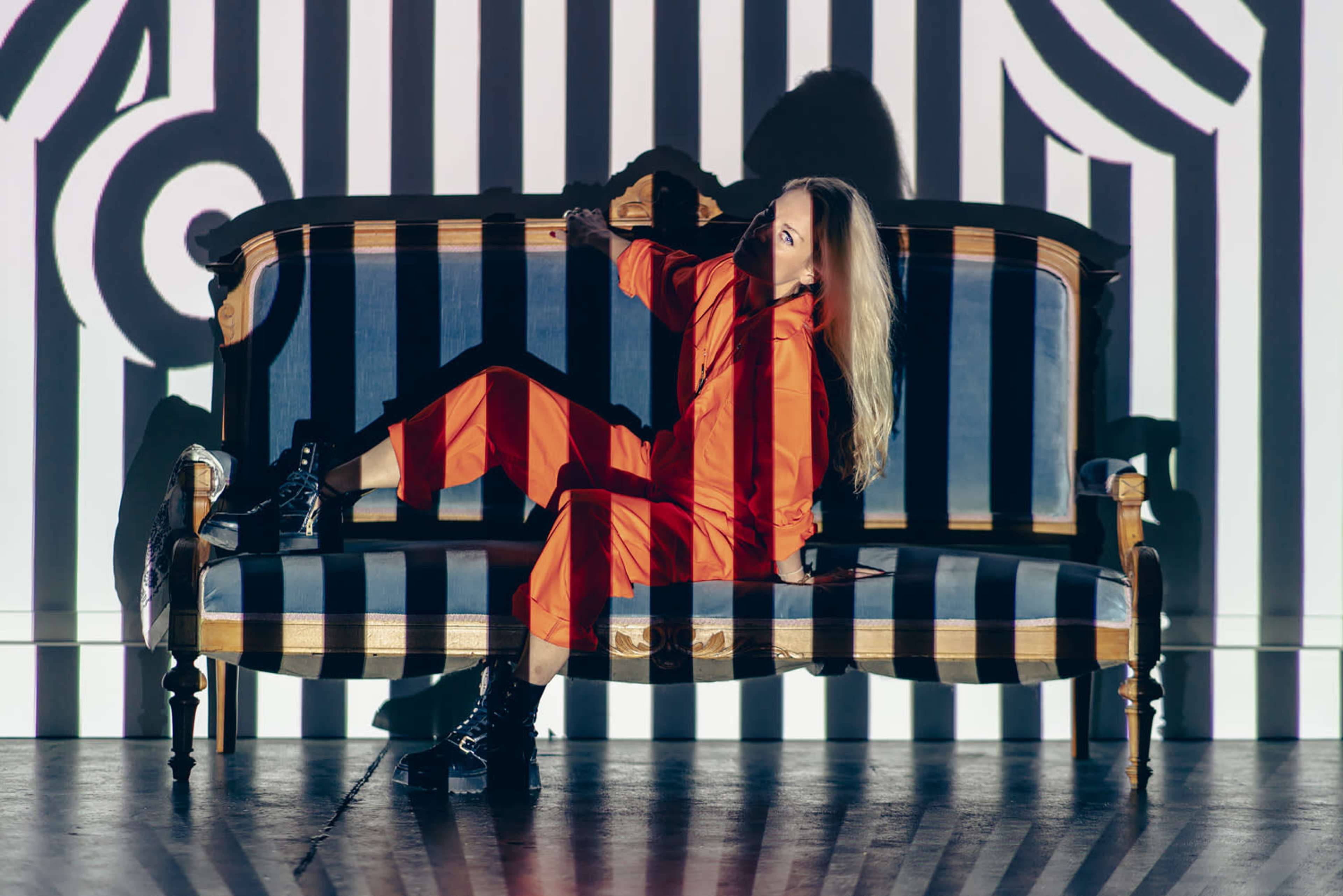 A person sits on a vintage couch against a backdrop of bold black and white stripes.
