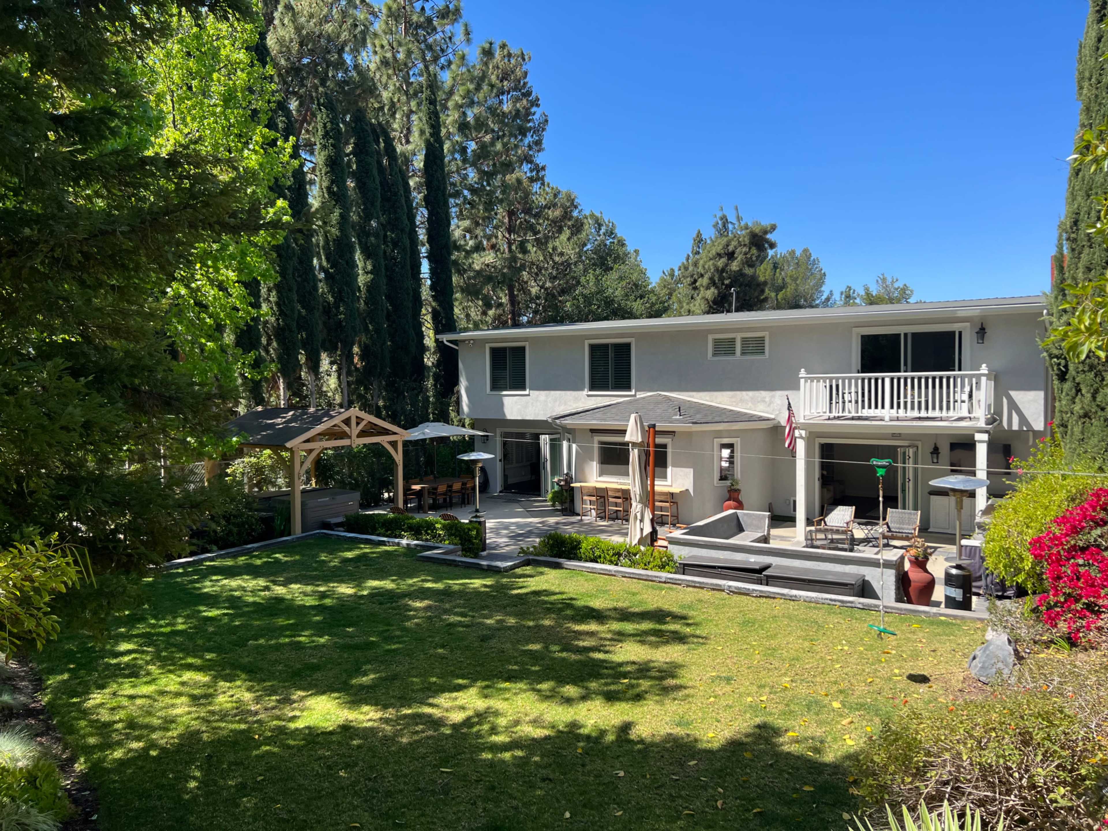 A two-story house with a patio, surrounded by a lawn and trees in a landscaped yard.