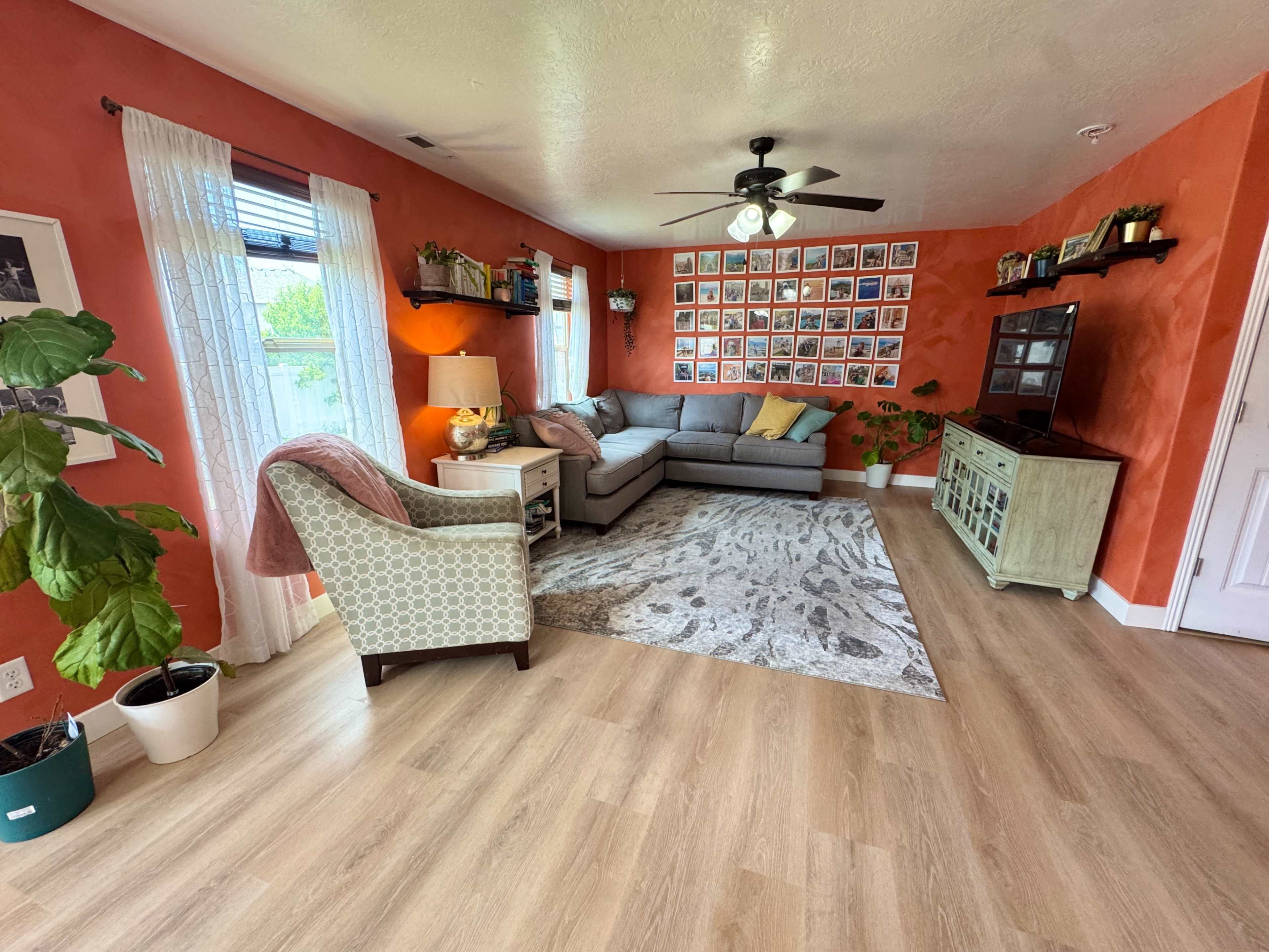 The living room features orange walls, a gray sectional sofa, and a gallery wall of framed photos, along with plants and hardwood flooring.