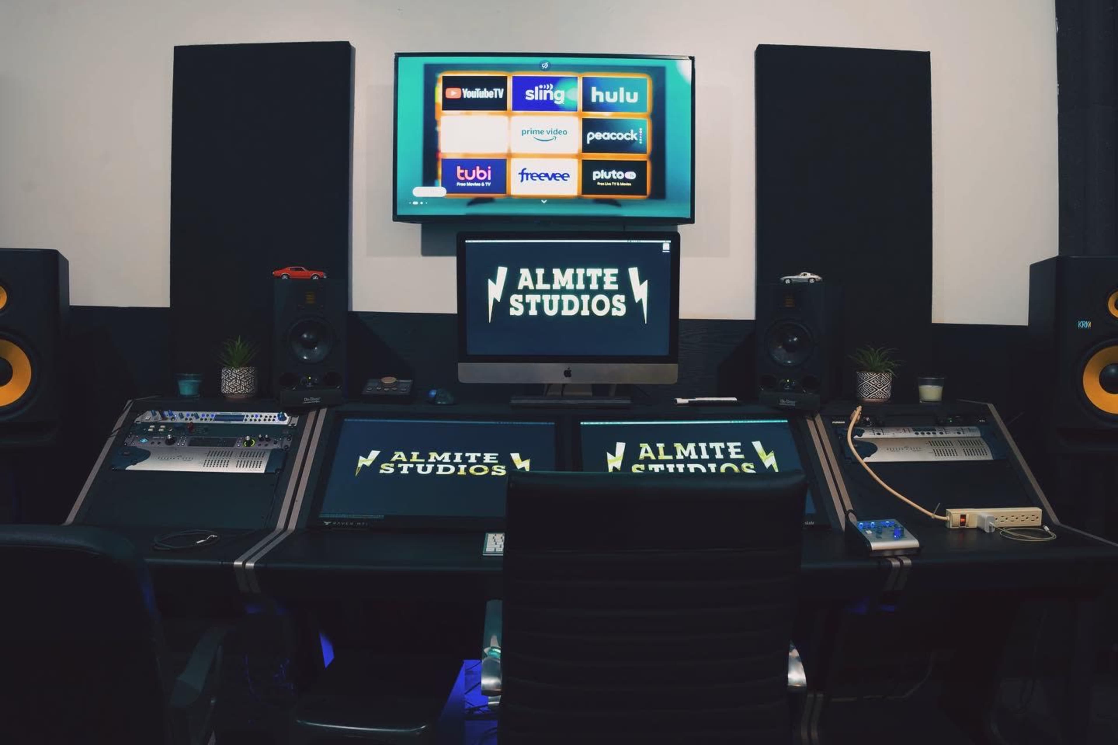 A modern sound recording studio with multiple screens, audio equipment, and branded signage for "ALMITE STUDIOS."