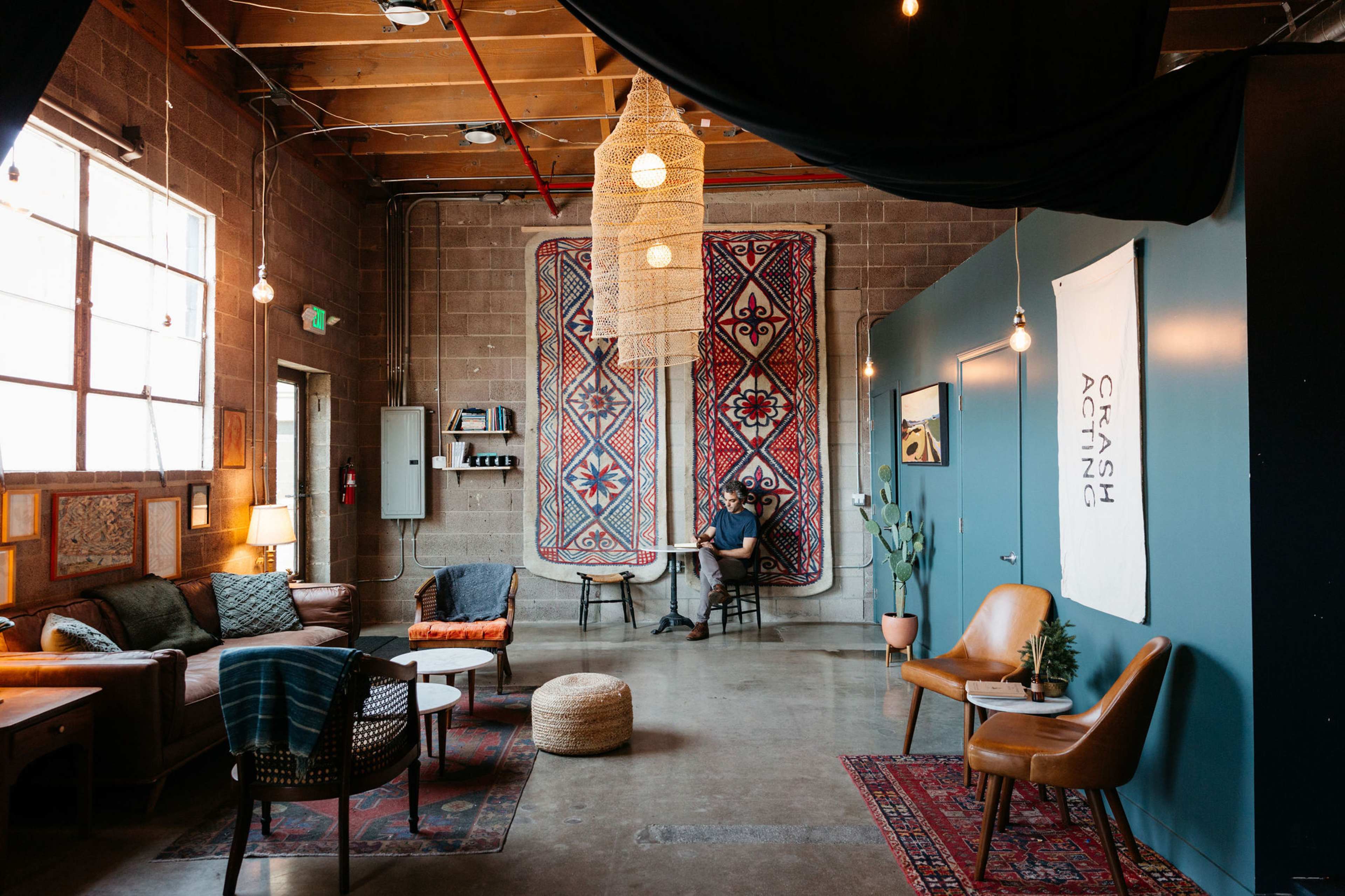 A person sits in a cozy urban lounge with patterned rugs, exposed brick walls, and hanging light fixtures.