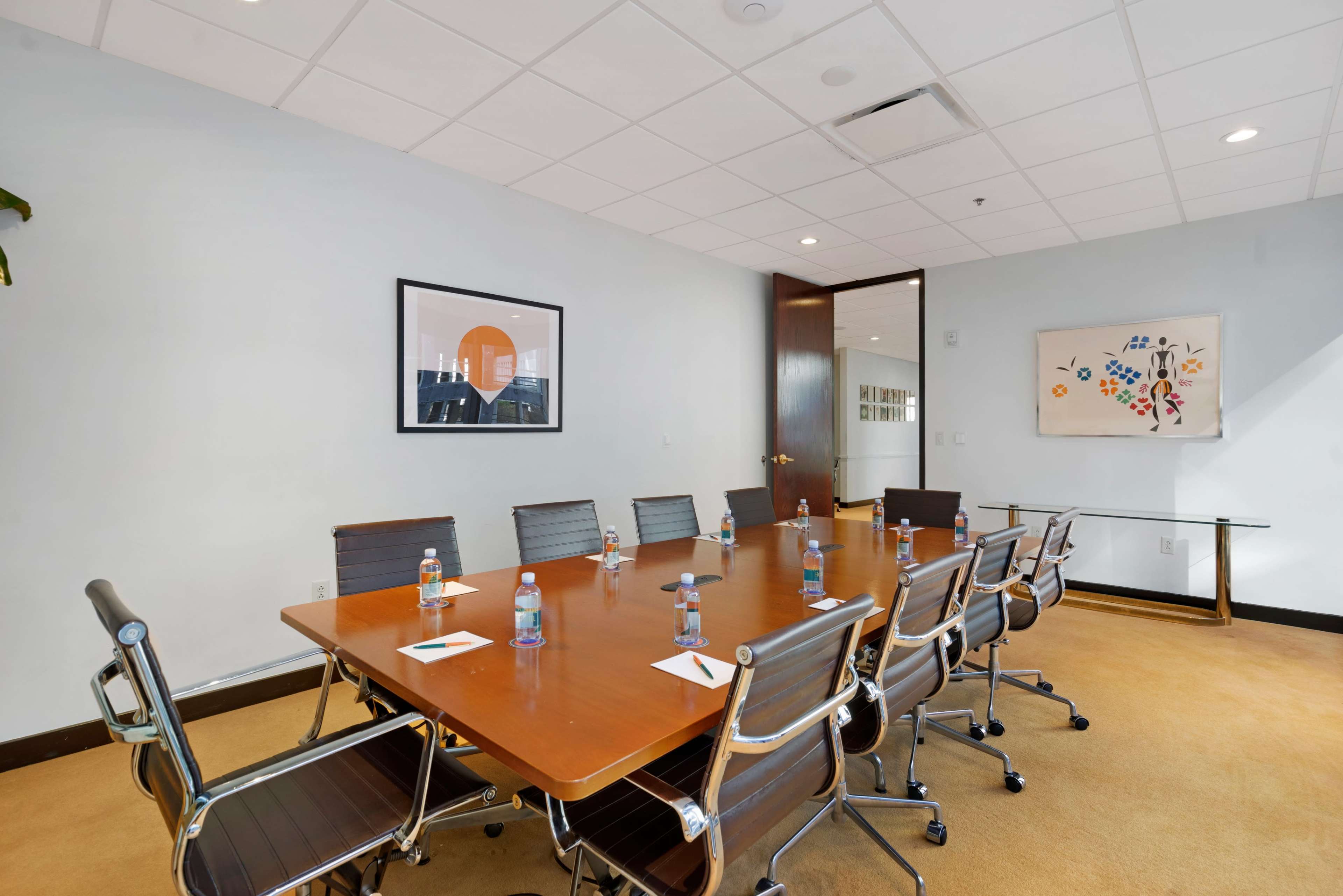 A conference room features a large wooden table surrounded by silver chairs, with water bottles and notepads placed at each seat.