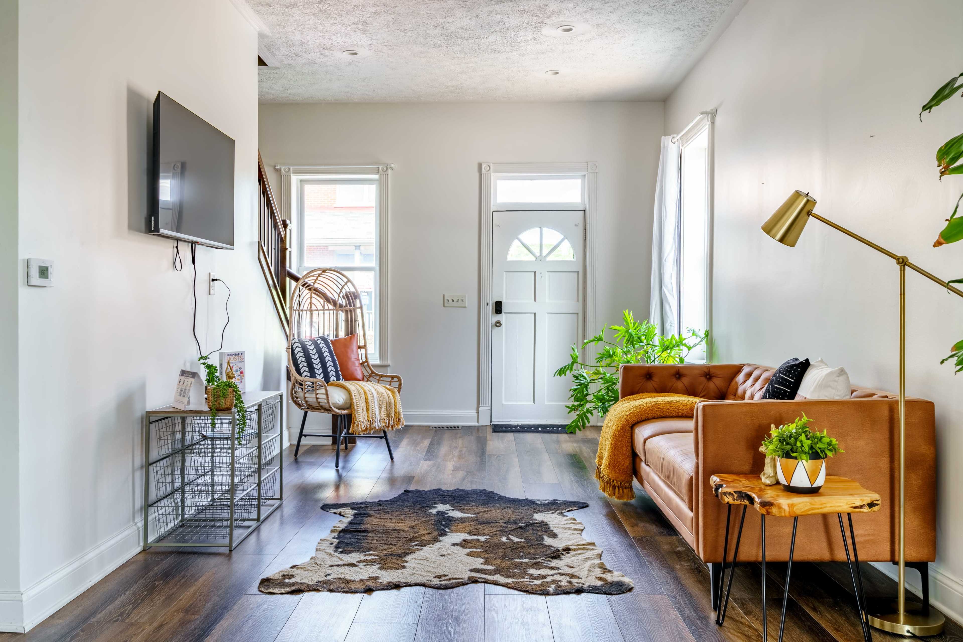 The image shows a bright living area featuring a brown leather sofa, a decorative chair, a small side table, and a door leading outside.