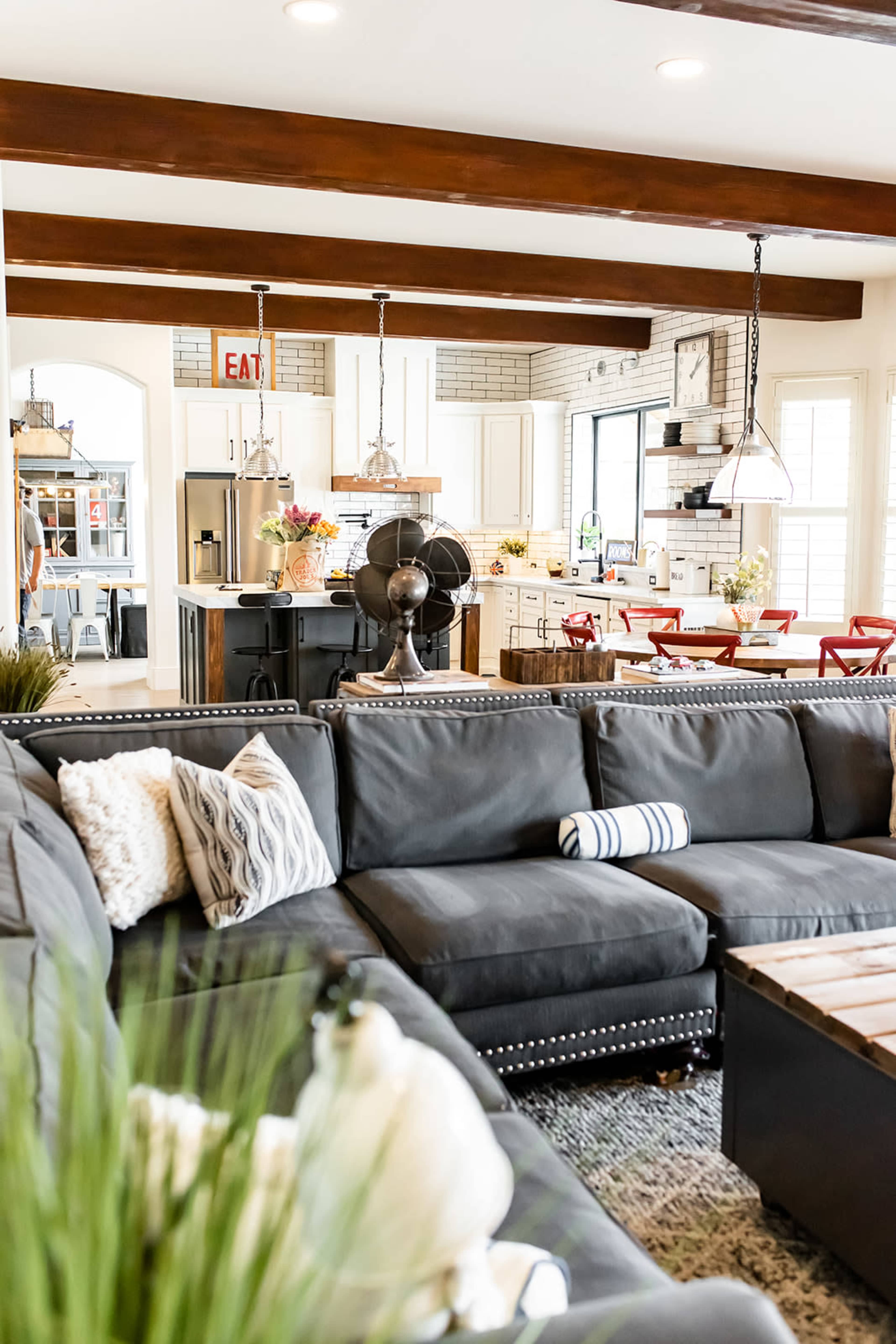 A spacious living room features a gray sectional sofa, a coffee table made of wood, and a view of a modern kitchen in the background.