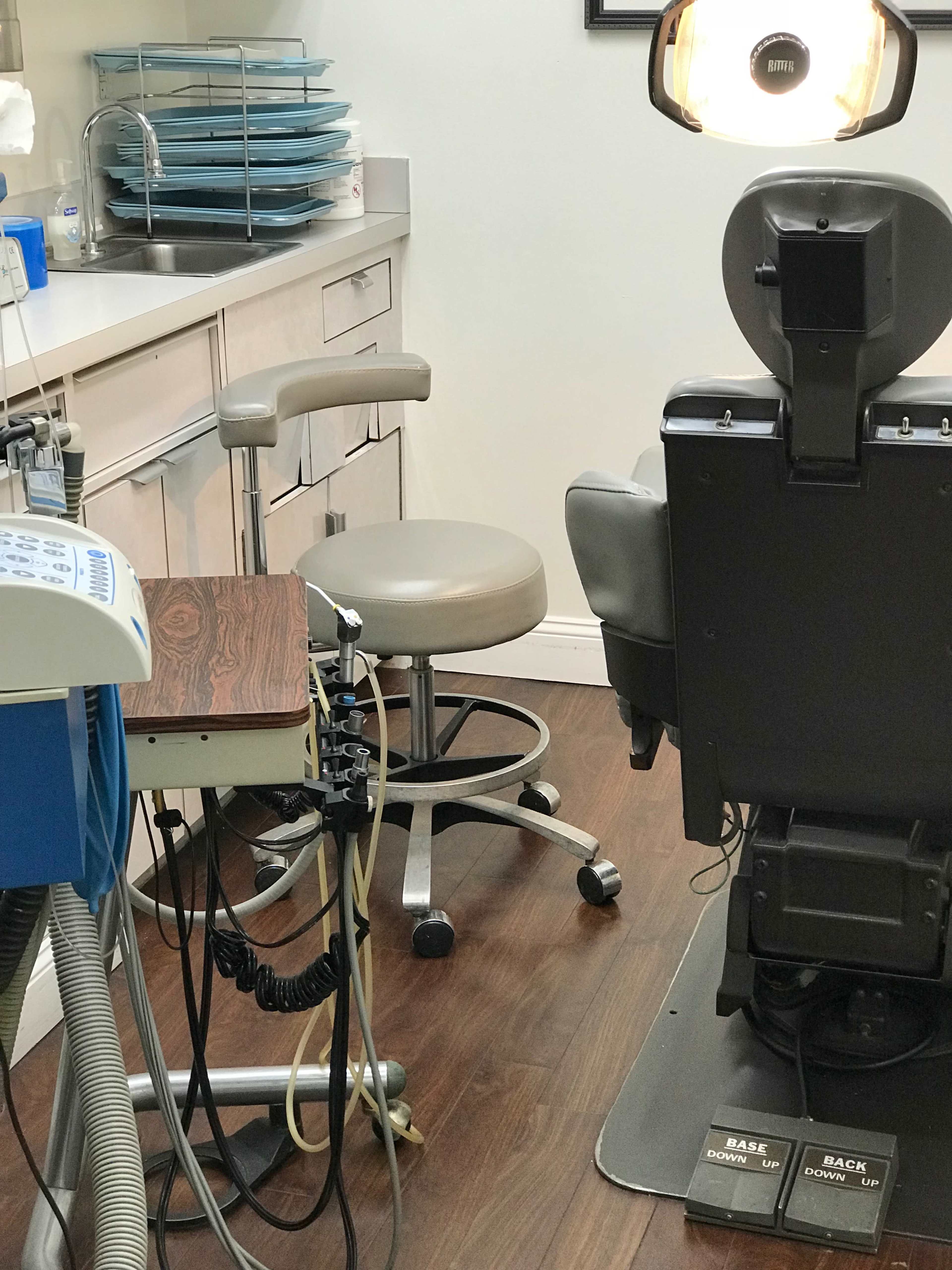 A dental office with a dental chair, a stool, and various equipment on a counter.