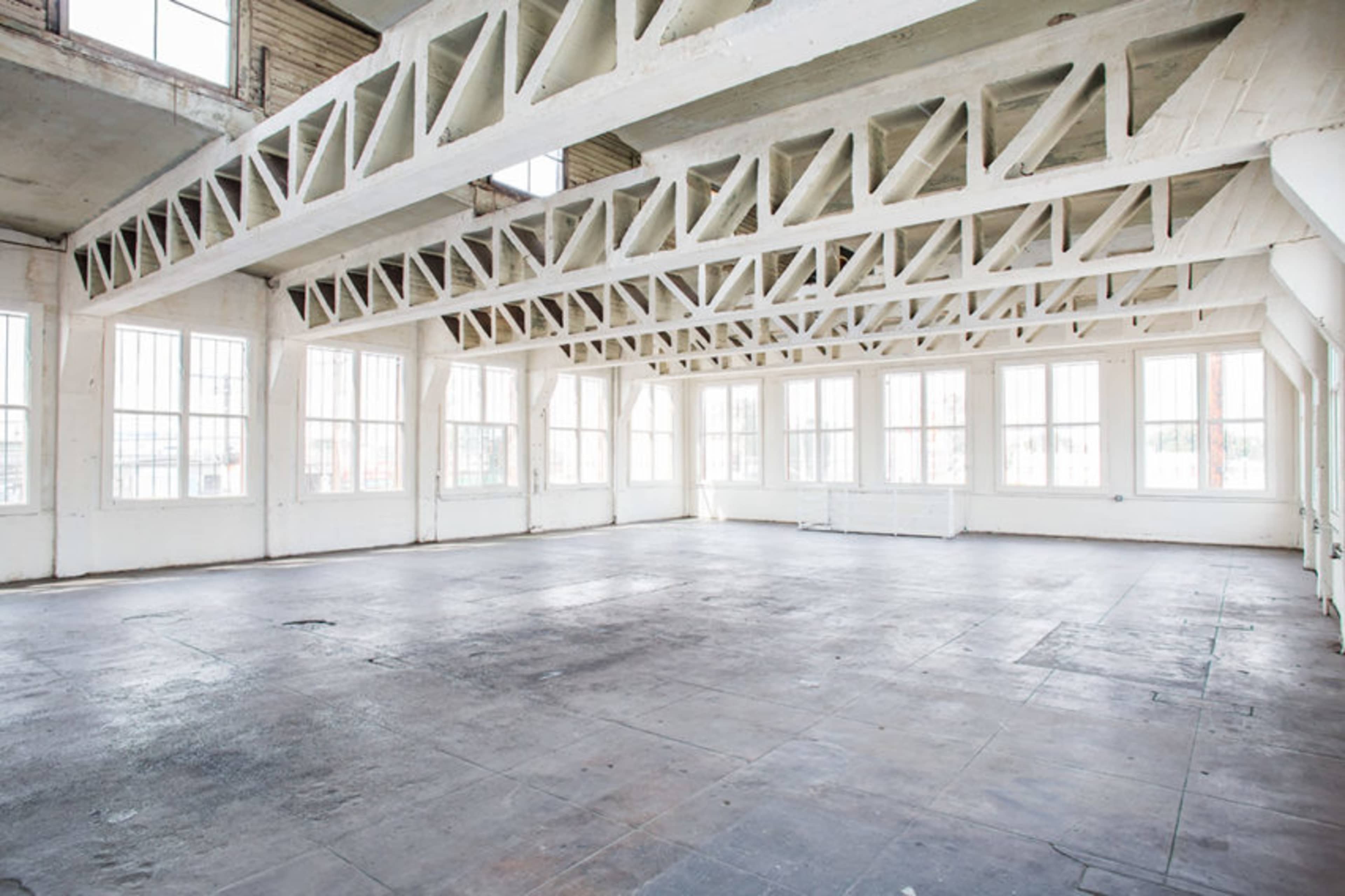A spacious, empty room with large windows and a high ceiling supported by exposed wooden beams.