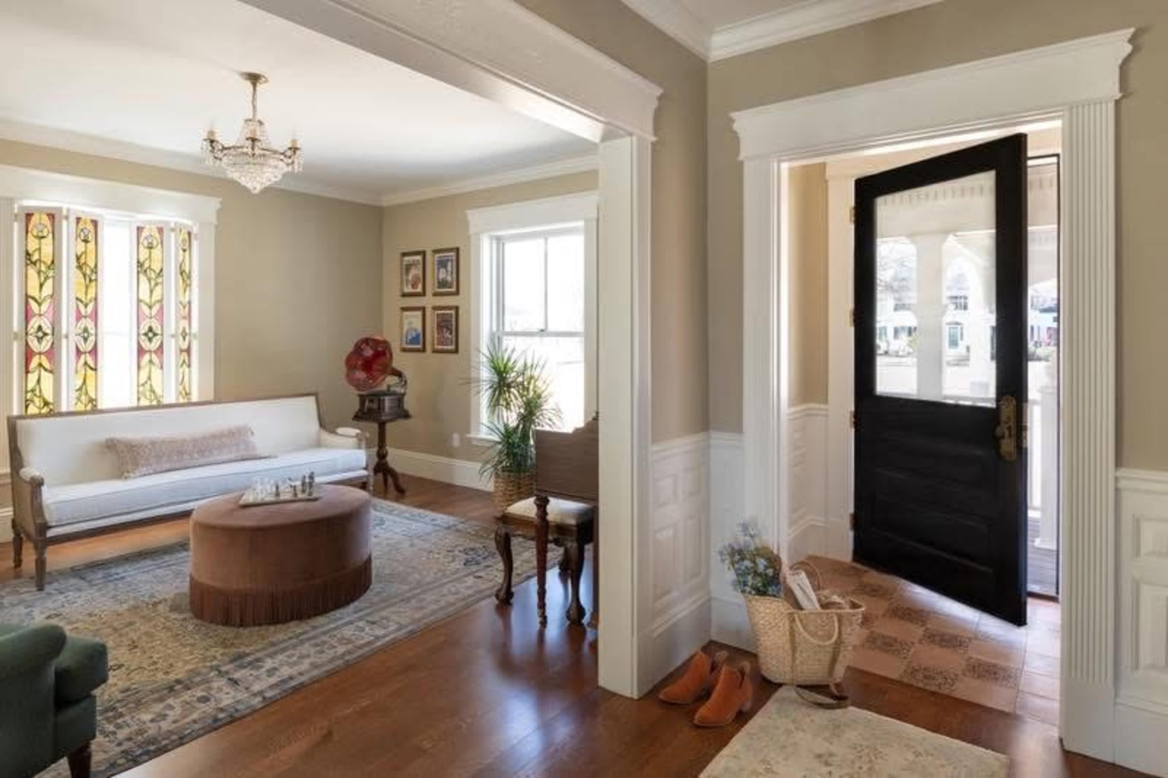 The image shows a well-lit foyer leading into a living room, featuring a white sofa, a round coffee table, and stained glass windows.
