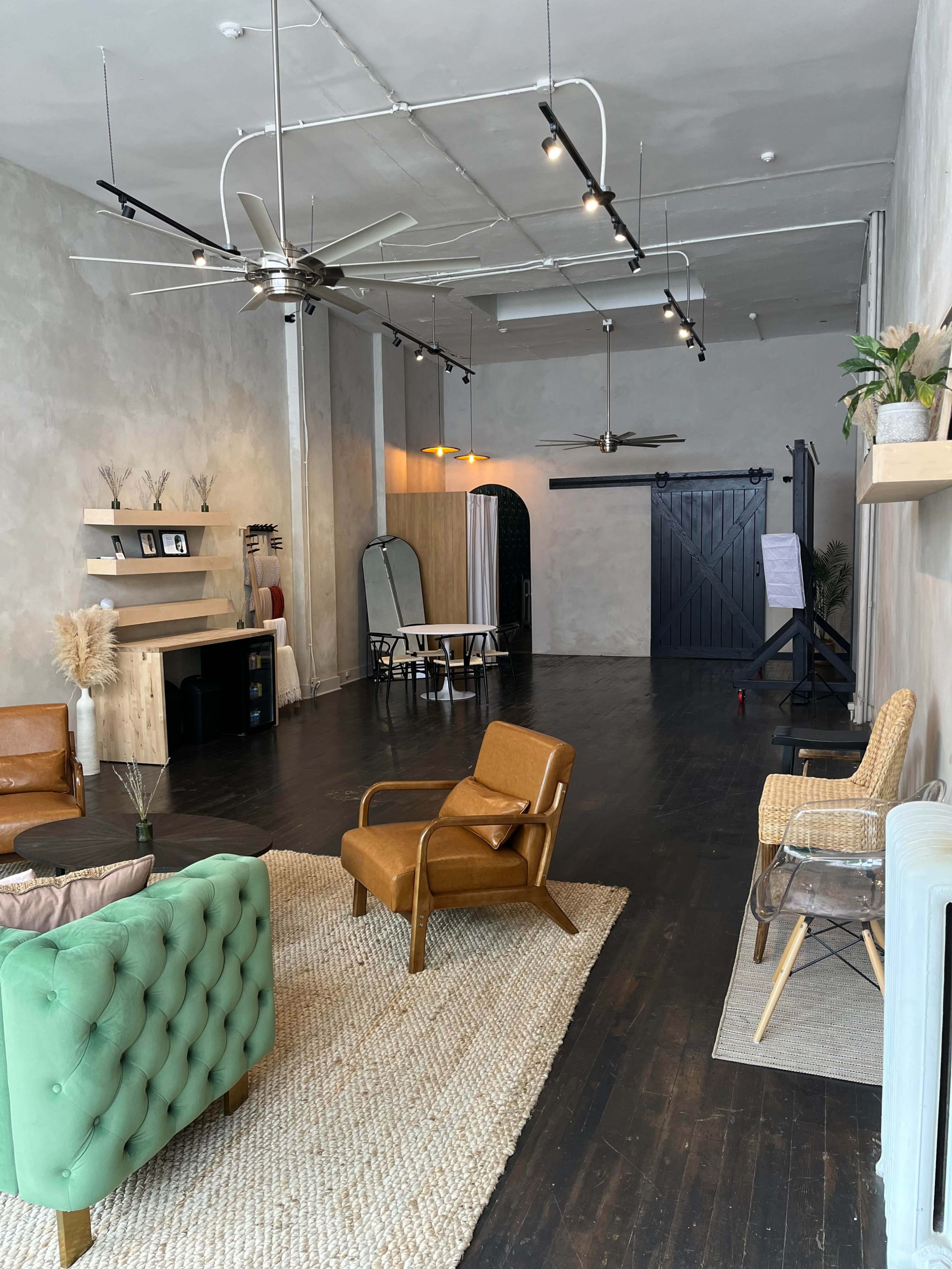 A spacious, minimally decorated room with a mix of seating areas, a large mirror, and a black door at the back.