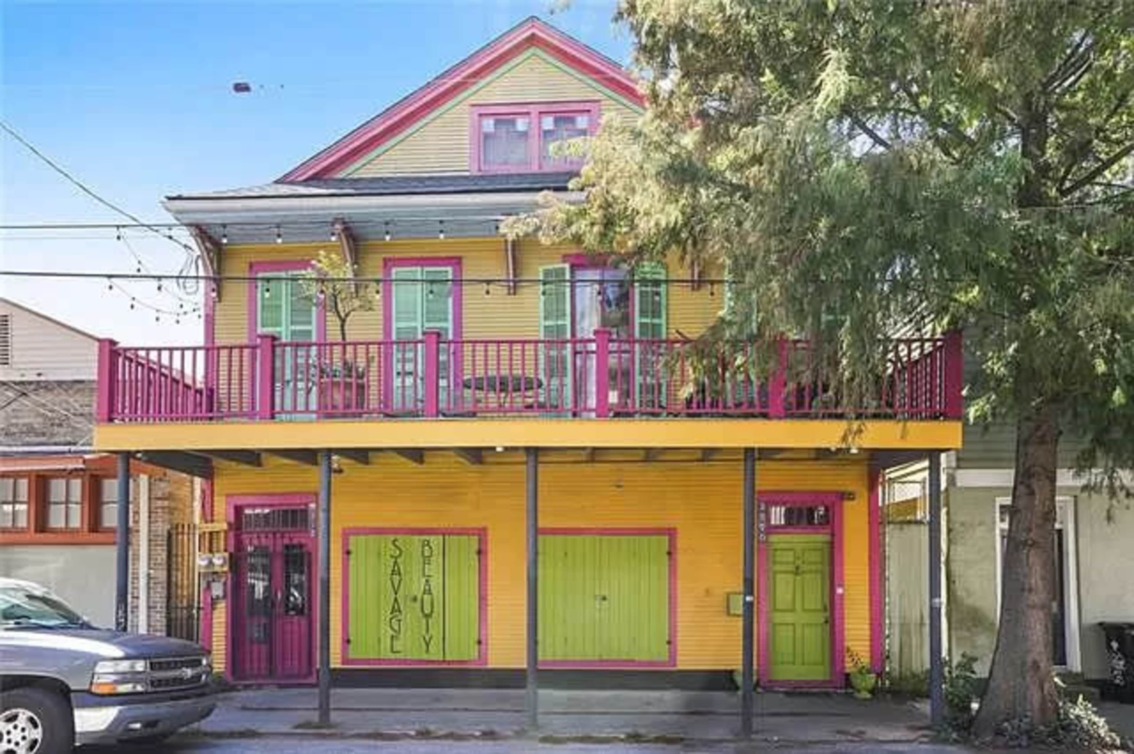 A brightly painted two-story house features colorful shutters and a balcony, situated next to a parked truck.