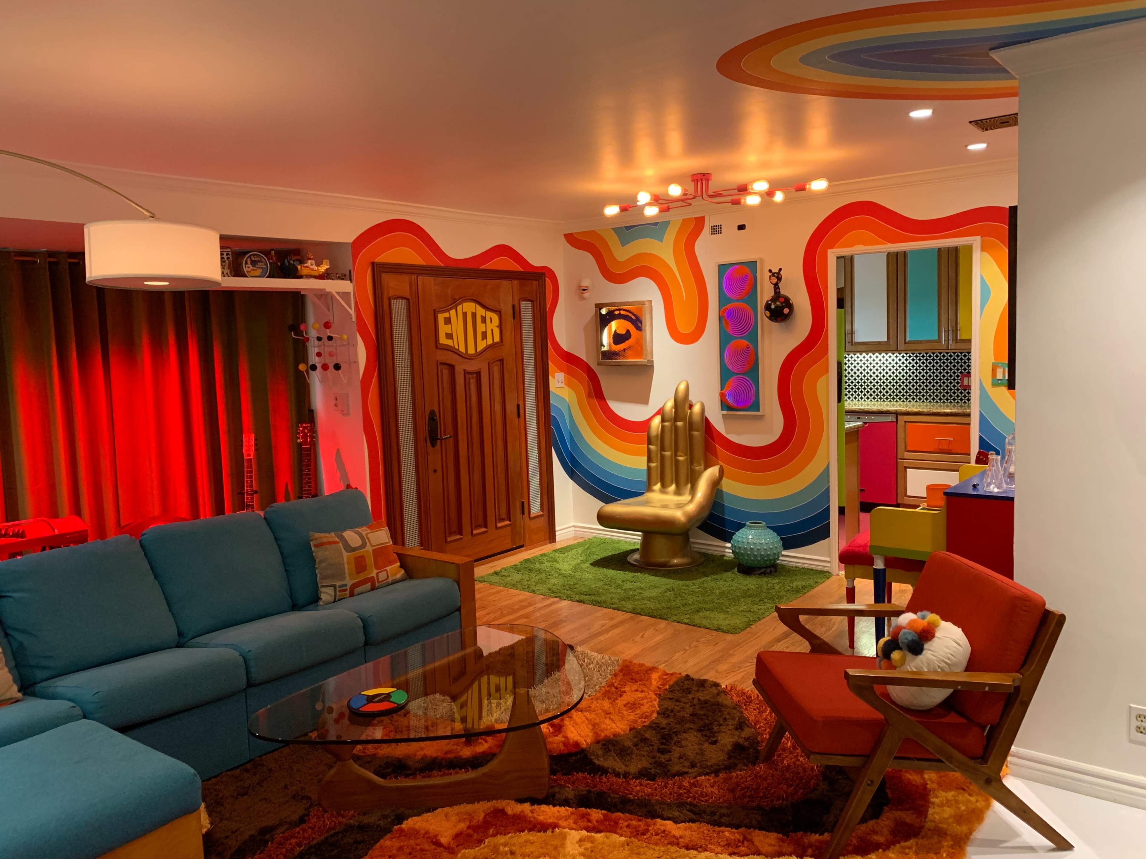A brightly colored living room with a rainbow-striped wall, a golden hand-shaped chair, and a mix of modern furniture.