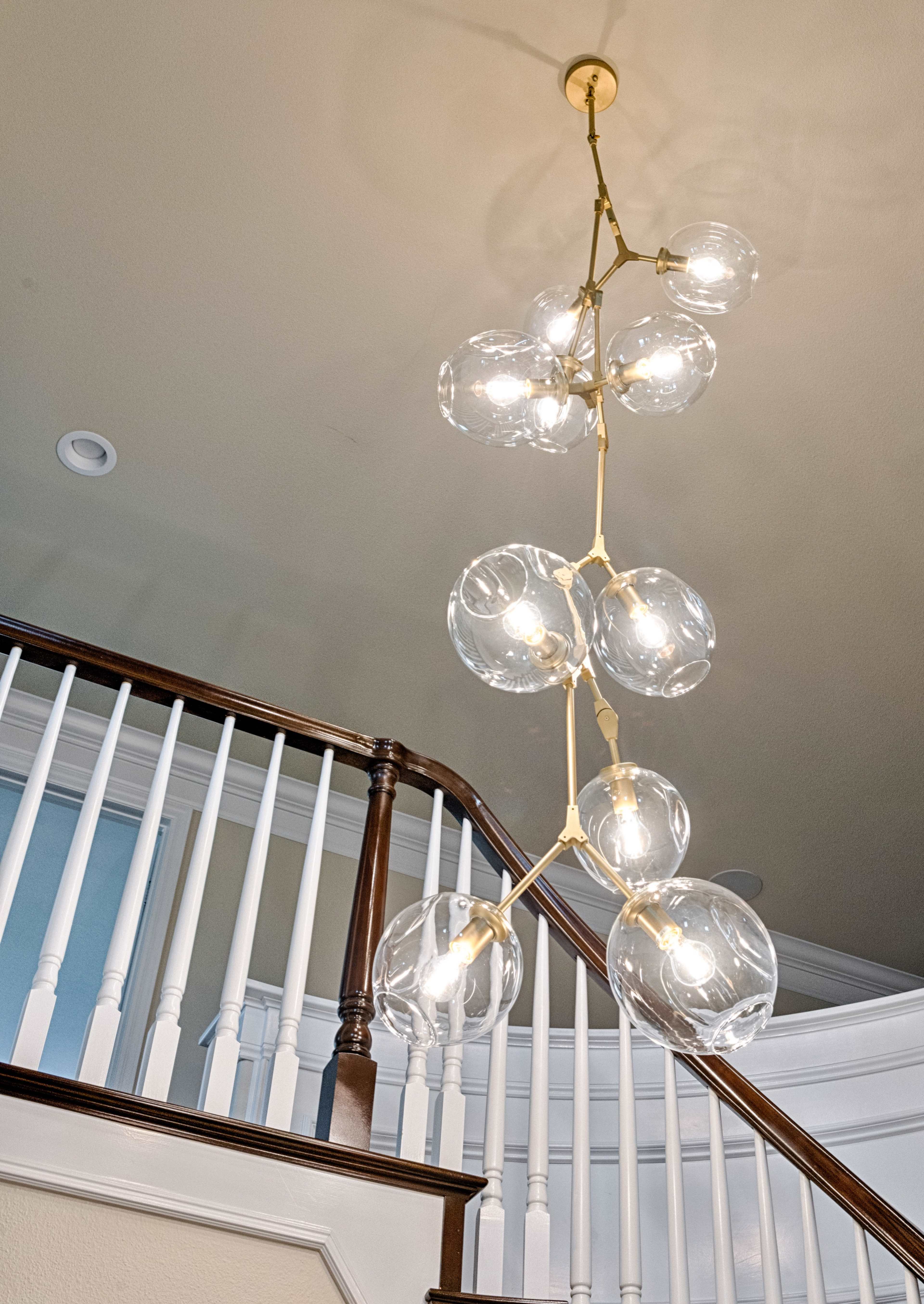 A modern light fixture with multiple clear globe bulbs hangs from a ceiling above a staircase with white railings.