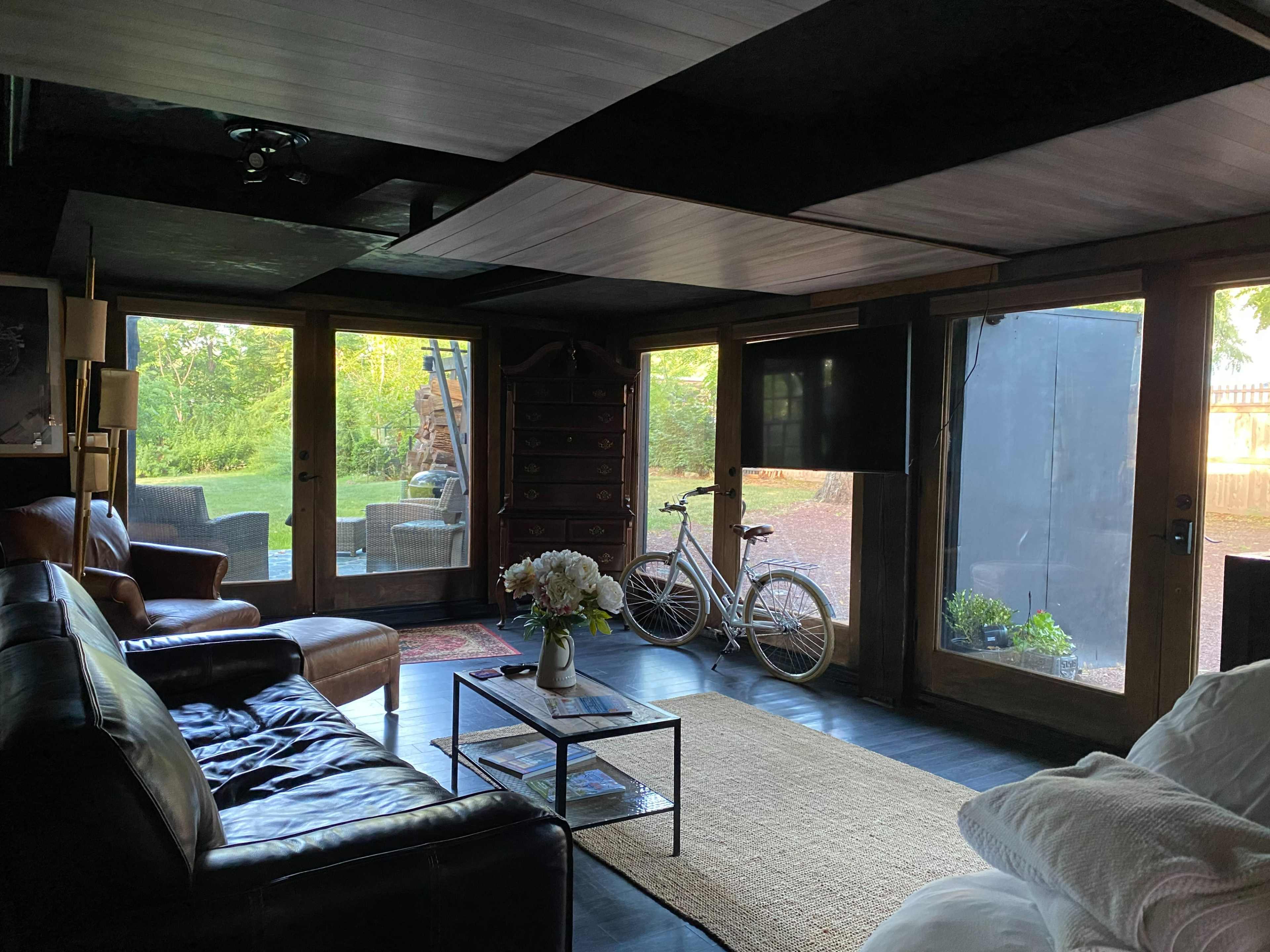 A cozy living room features leather sofas, a glass coffee table, and windows that overlook a backyard with a bicycle parked nearby.