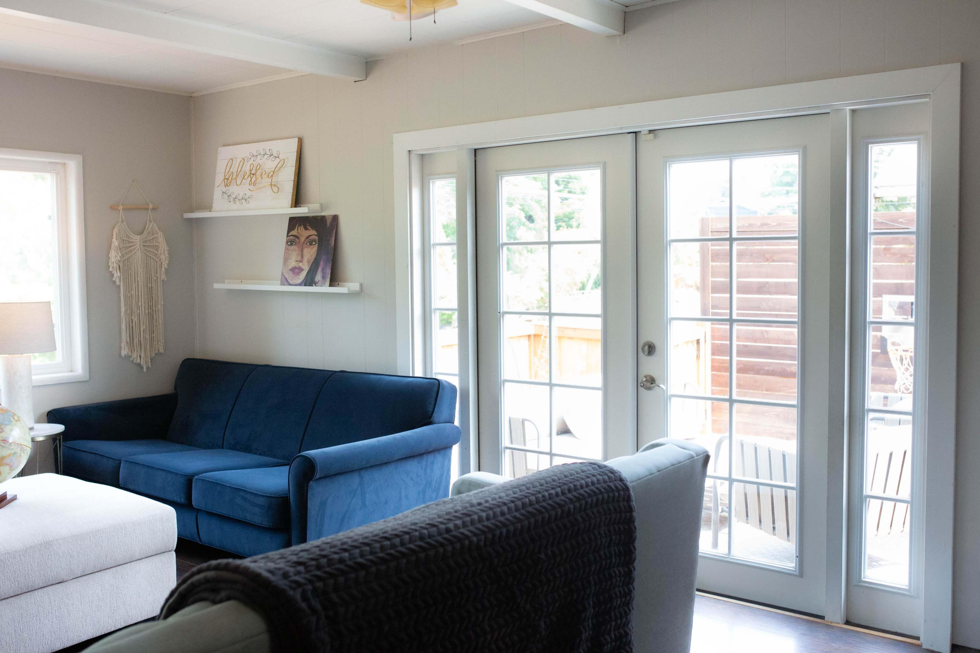 The image shows a cozy living room with a blue sofa, a beige couch, and large glass doors leading to an outdoor space.